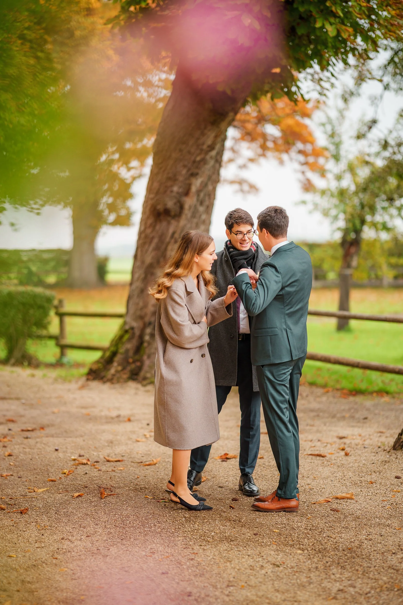 Drei Menschen stehen im Park, lachen und unterhalten sich. Es ist Herbst, die Bäume haben bunte Blätter, und der Boden ist bedeckt mit Laub.
