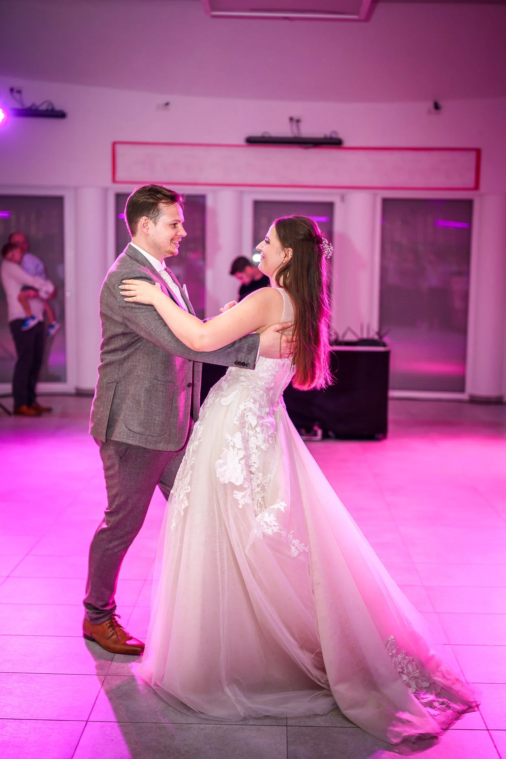 Ein Brautpaar tanzt auf einer Hochzeitsfeier, die Braut trägt ein weißes Hochzeitskleid, der Bräutigam einen grauen Anzug.