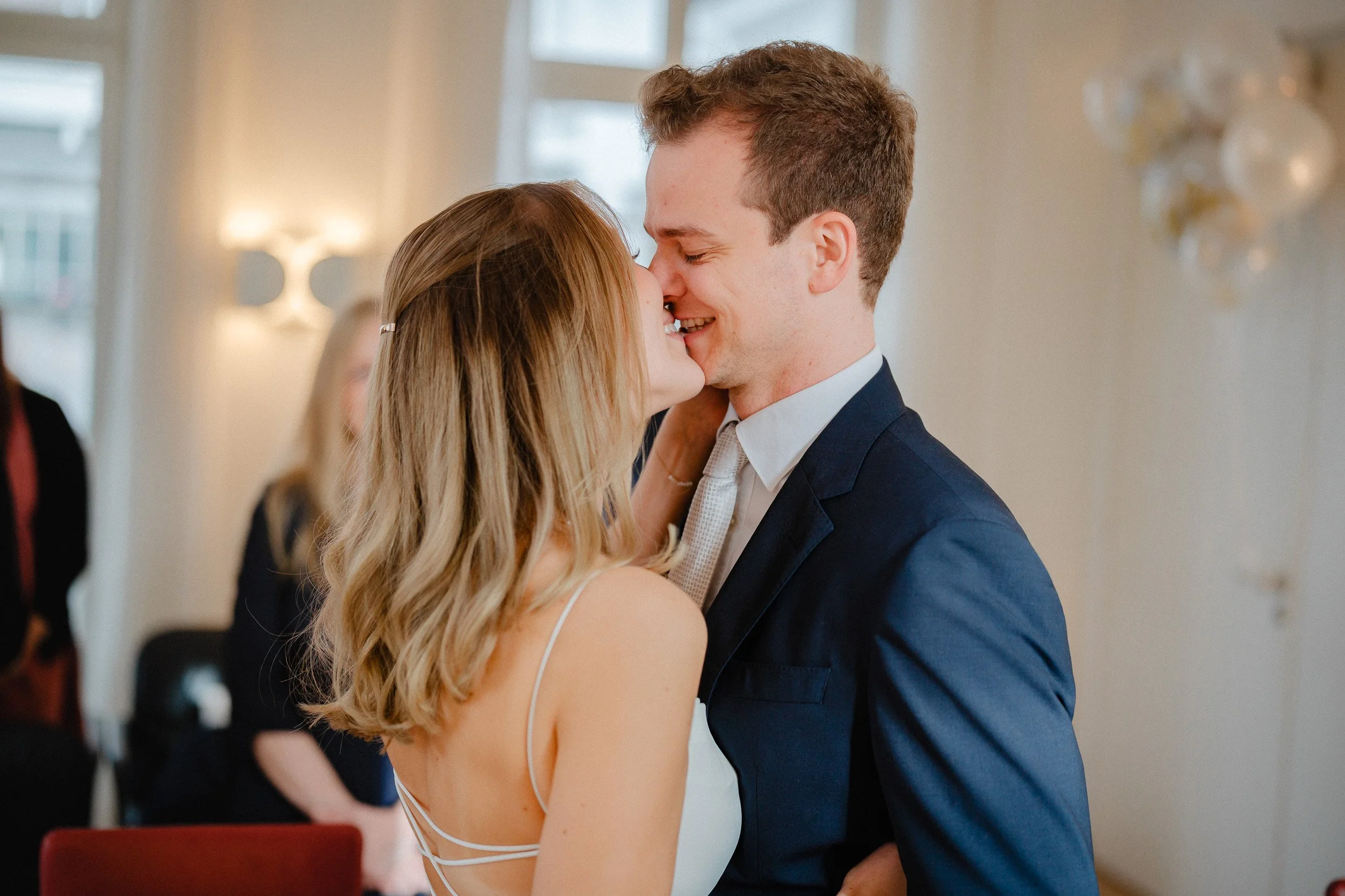 Ein junges Paar küsst sich bei einer Hochzeit in einem hell erleuchteten Raum.