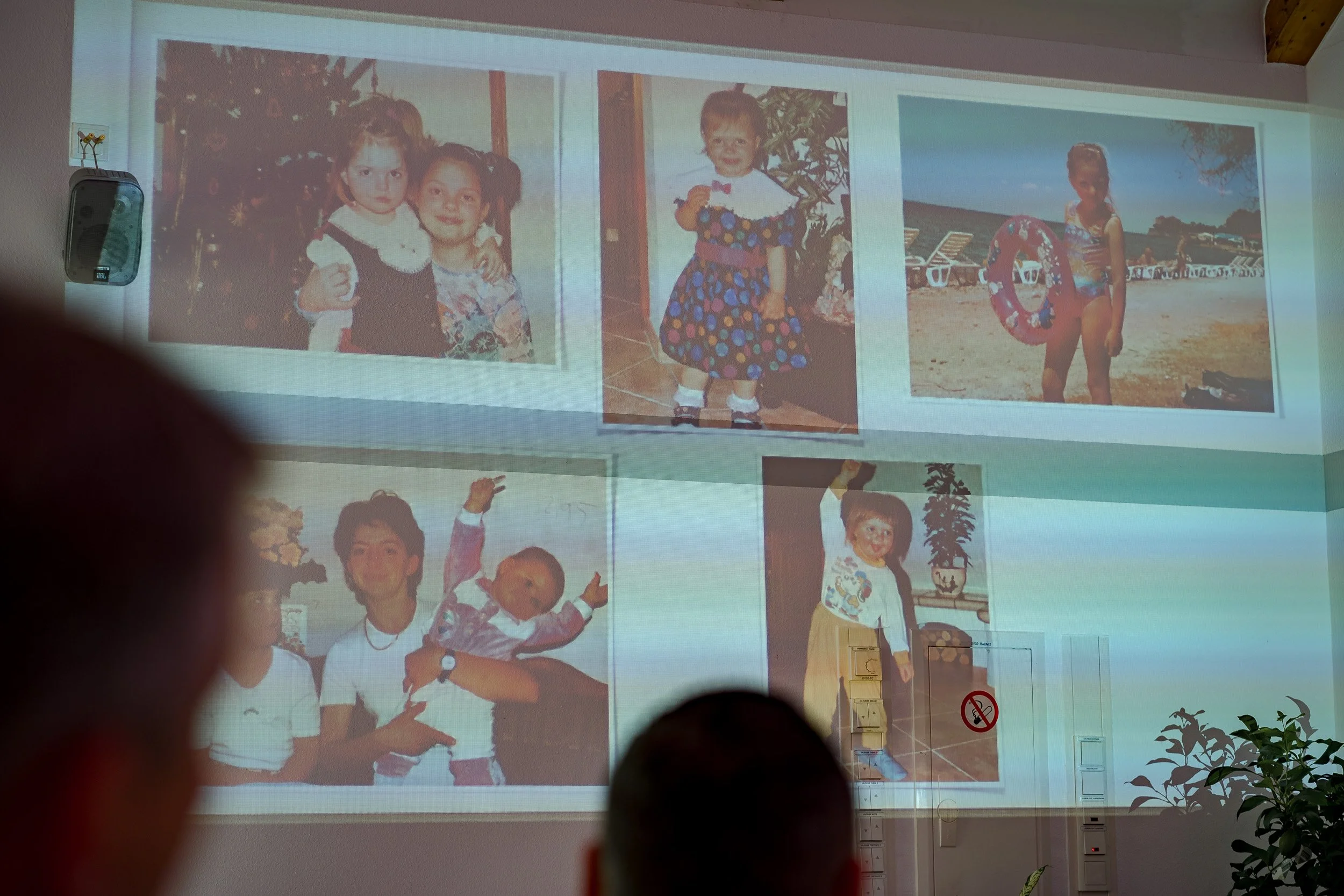 Eine Diashow mit Fotos von Kindern, die auf einer Leinwand projiziert werden, im Hintergrund ein Raum mit Pflanzen und einem 