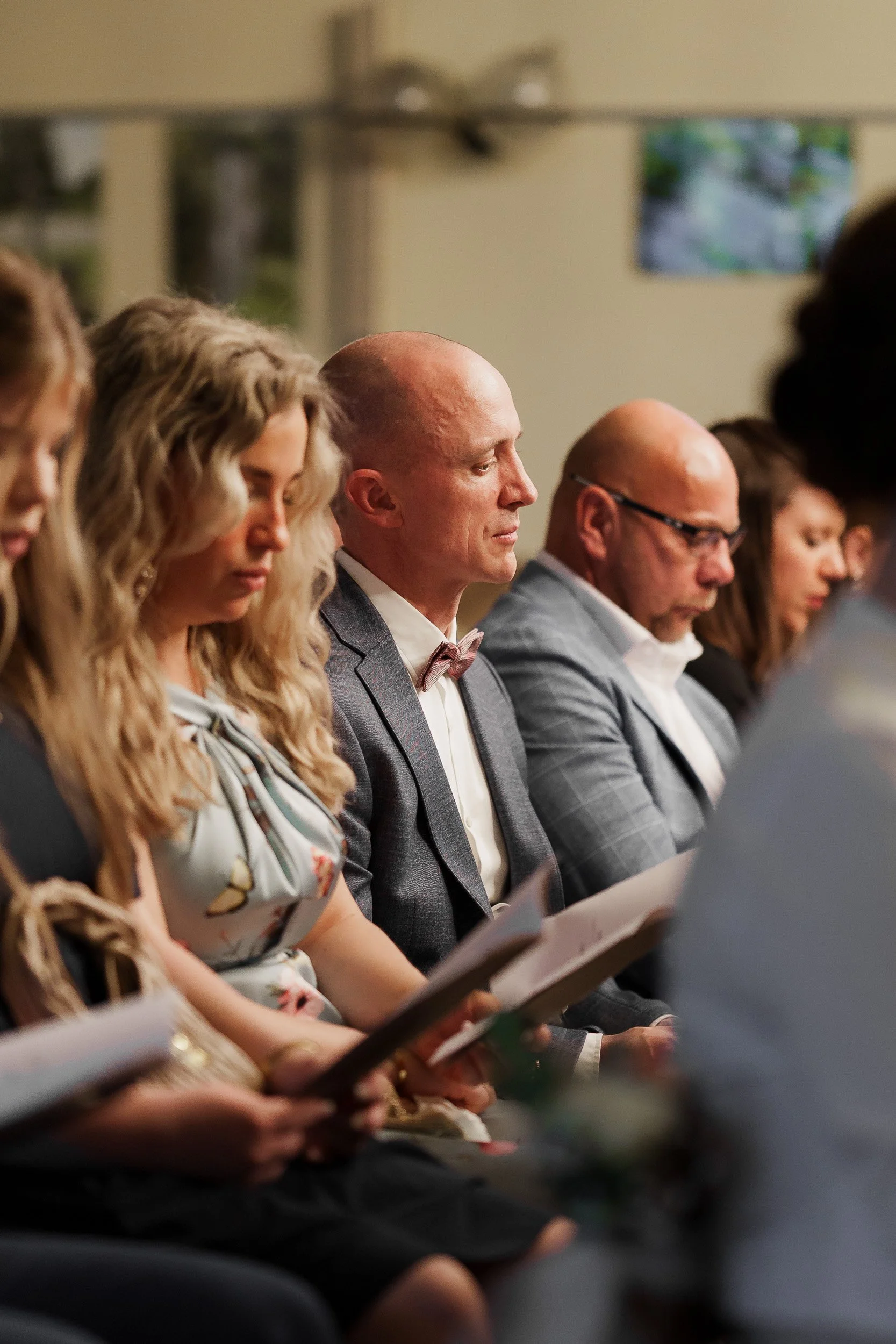 Menschen sitzen in einer Reihe bei einer formellen Veranstaltung, alle lesen Papiere und haben geschlossene Augen.