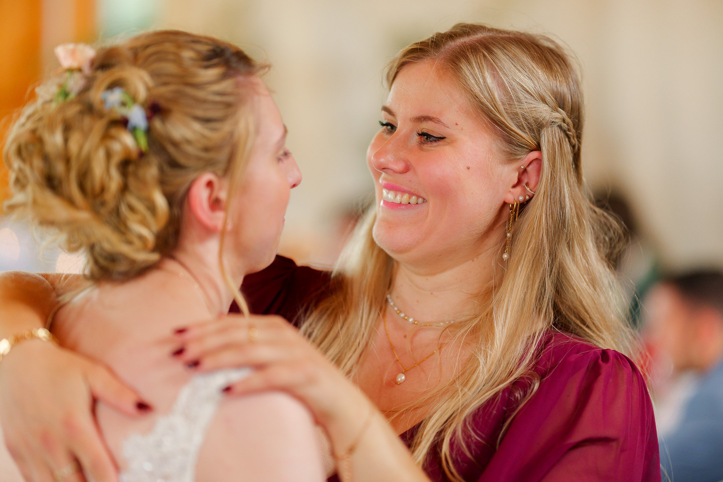Zwei Frauen umarmen sich, lächeln sich freundlich an, bei einer Feier oder Hochzeit.