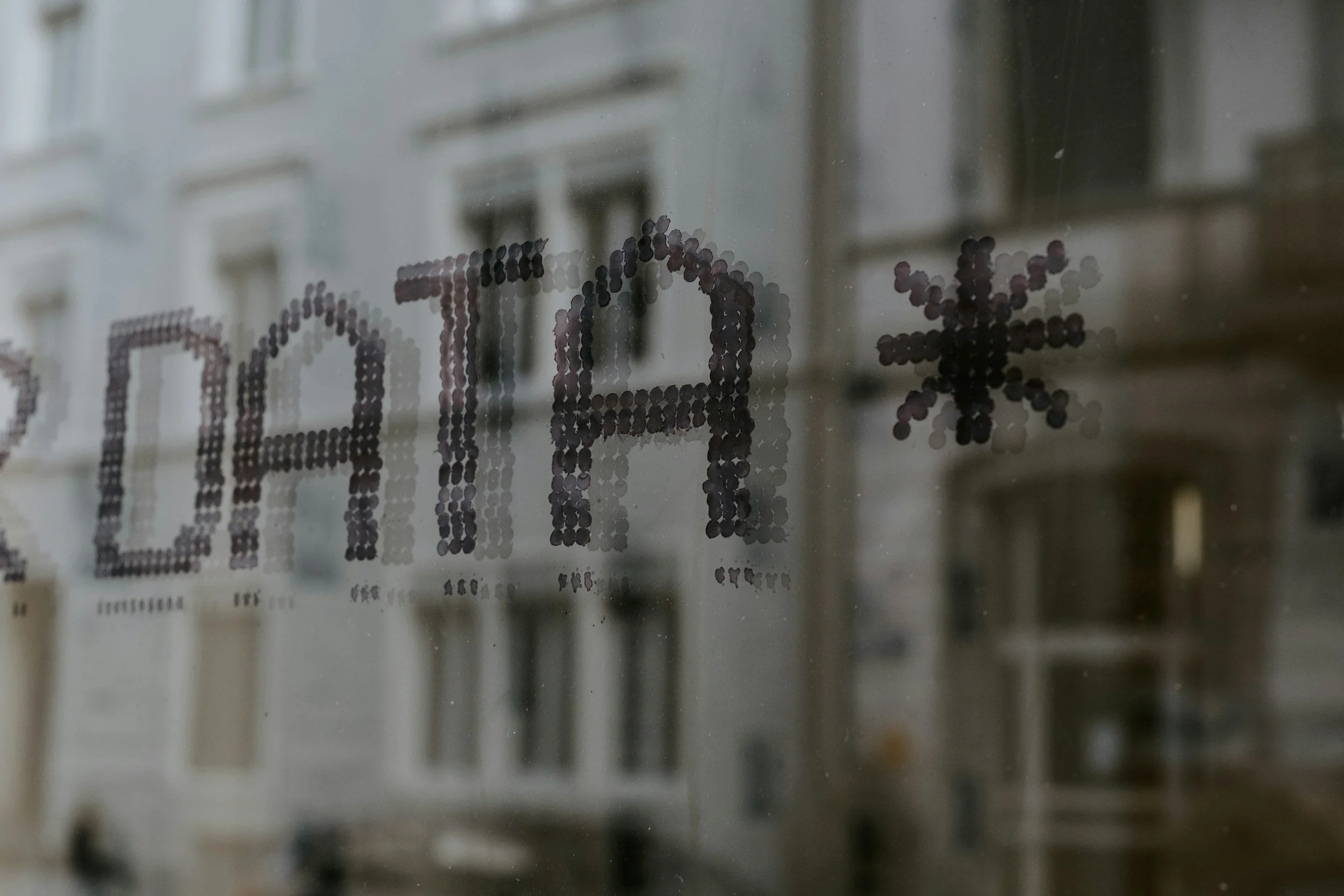 A window with the text 'OPEN' and a snowflake symbol, written in dot matrix style, reflected in the glass.