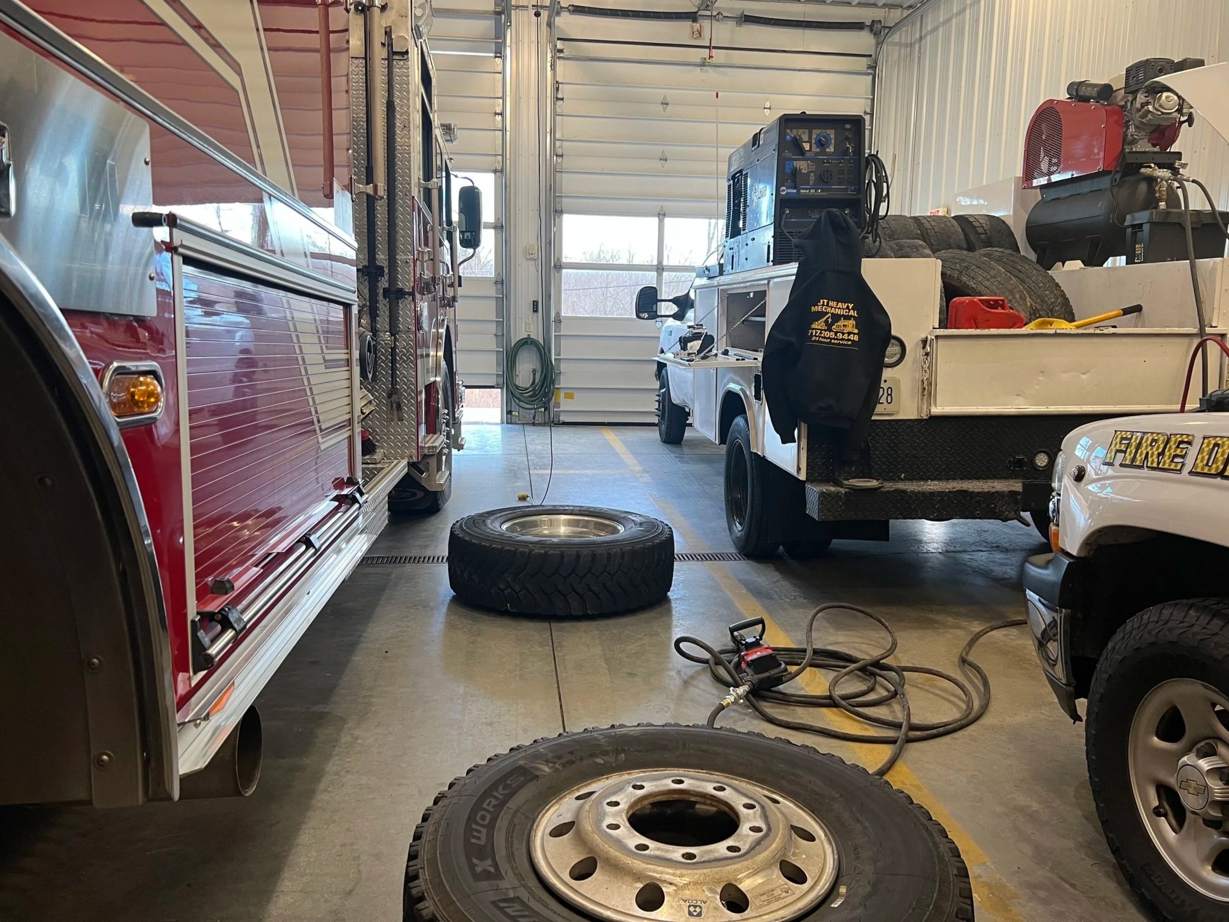 A garage with emergency rescue vehicles, including fire trucks and utility trucks, with tools, tires, and equipment scattered inside.