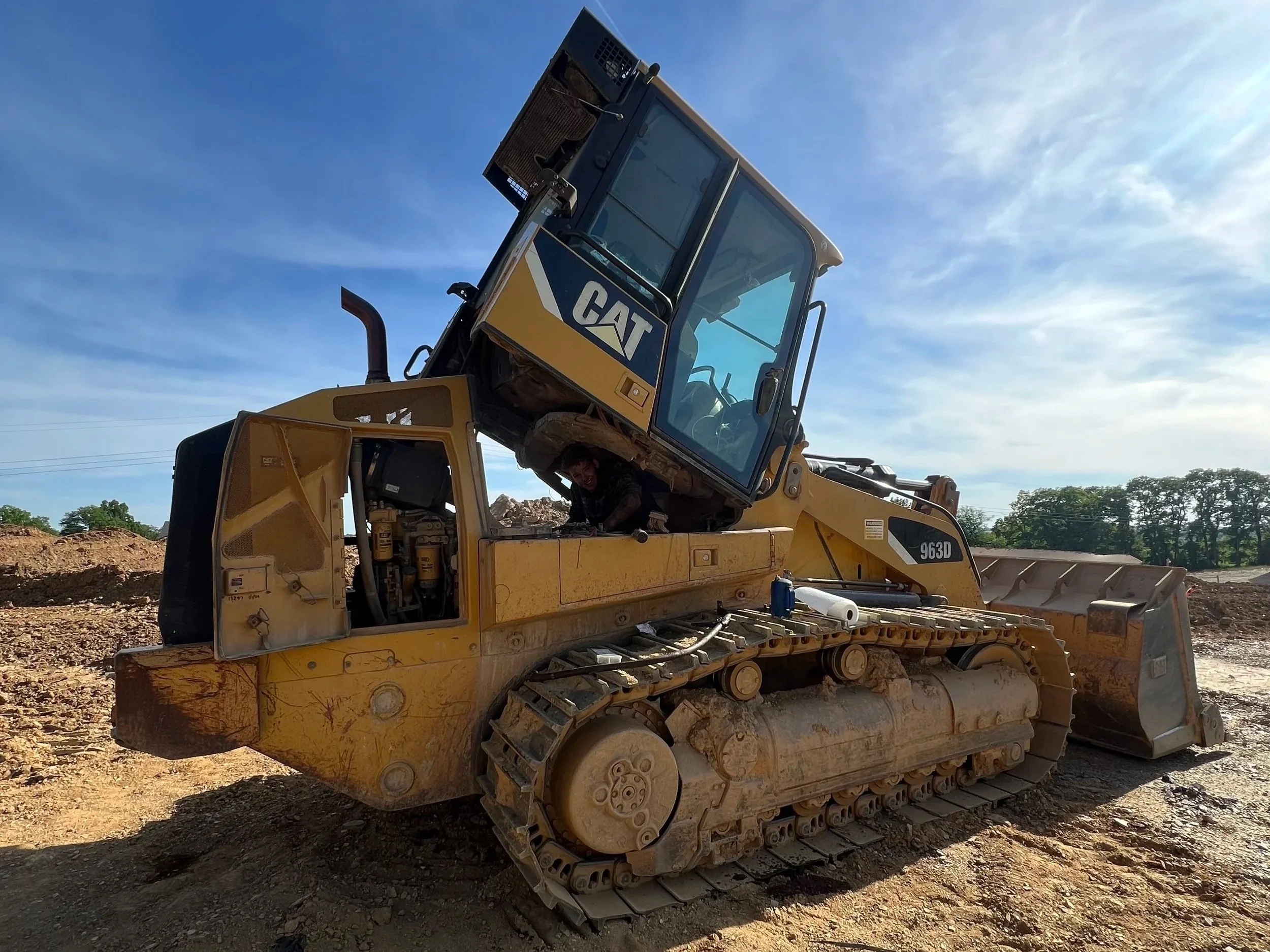 A yellow Caterpillar bulldozer on a construction site with a person inside the cabin, under a blue sky.