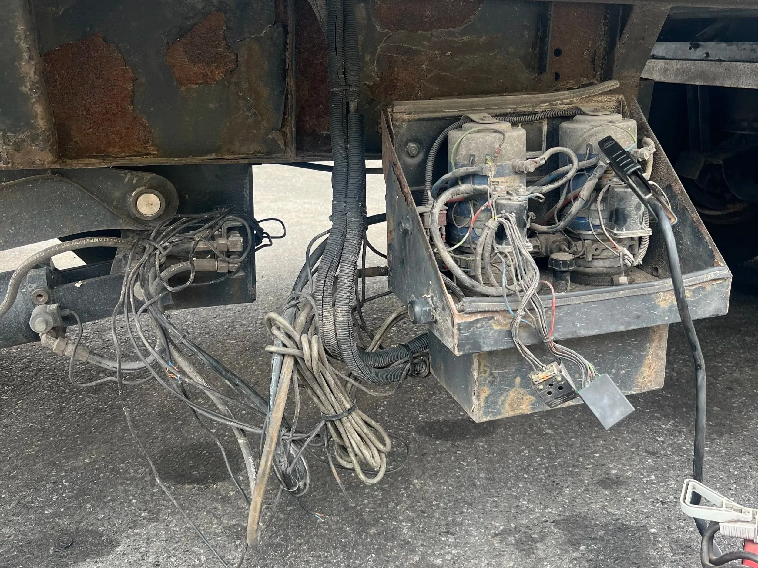 Close-up of an exposed vehicle engine compartment with wires, cables, and mechanical parts, showing rust and dirt on the metal surfaces.
