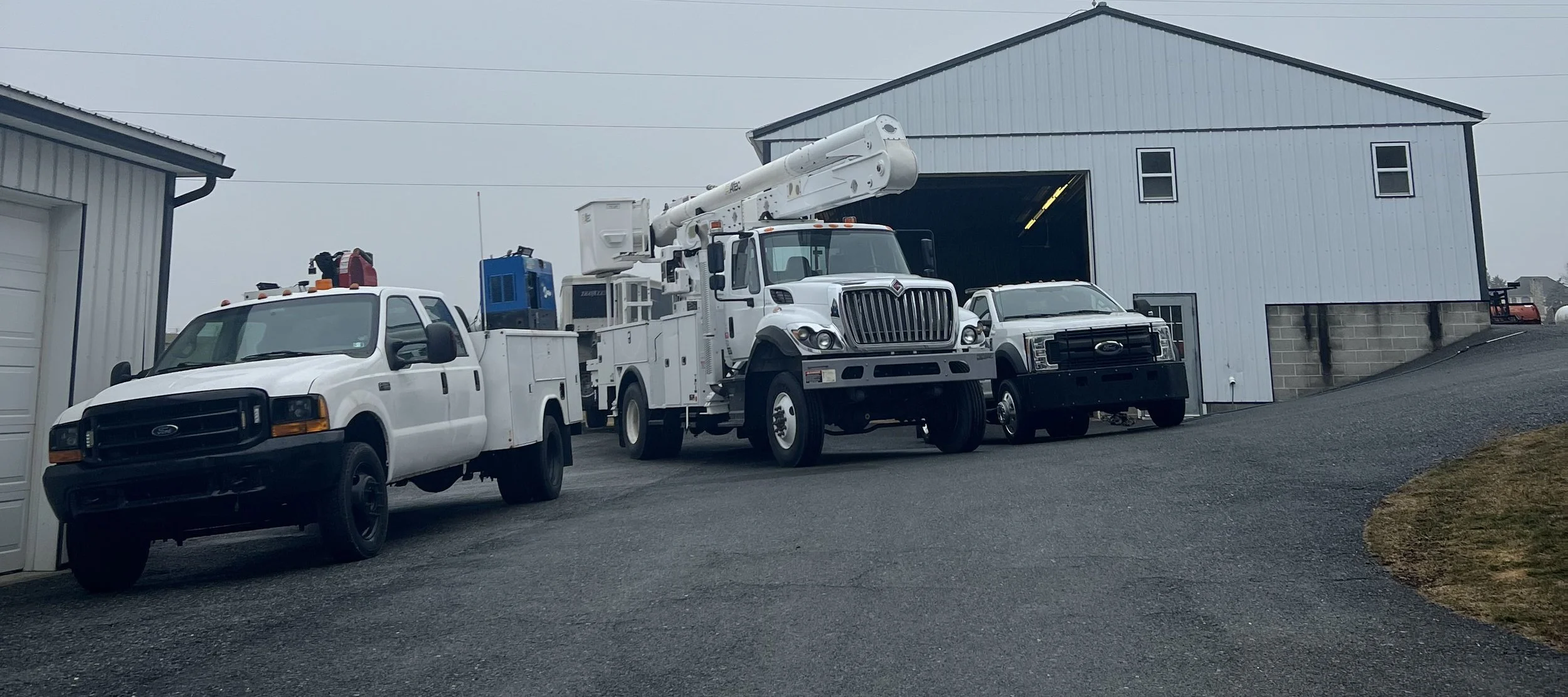 A fleet of utility trucks parked outside a large blue metal building on a cloudy day.