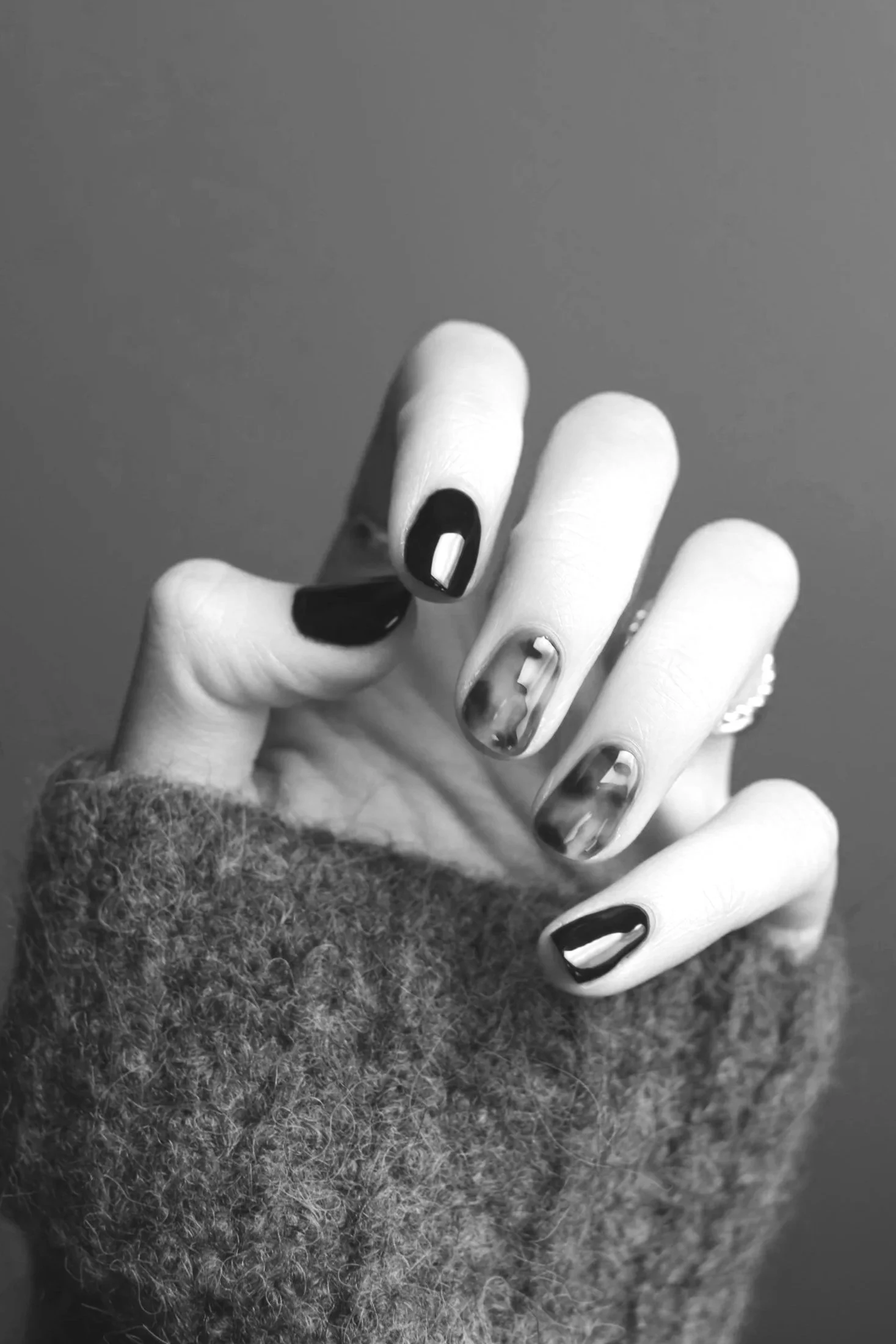 Close-up of a hand with manicured nails, some painted black and some with marble design, partially covered by a fuzzy sweater in black and white.