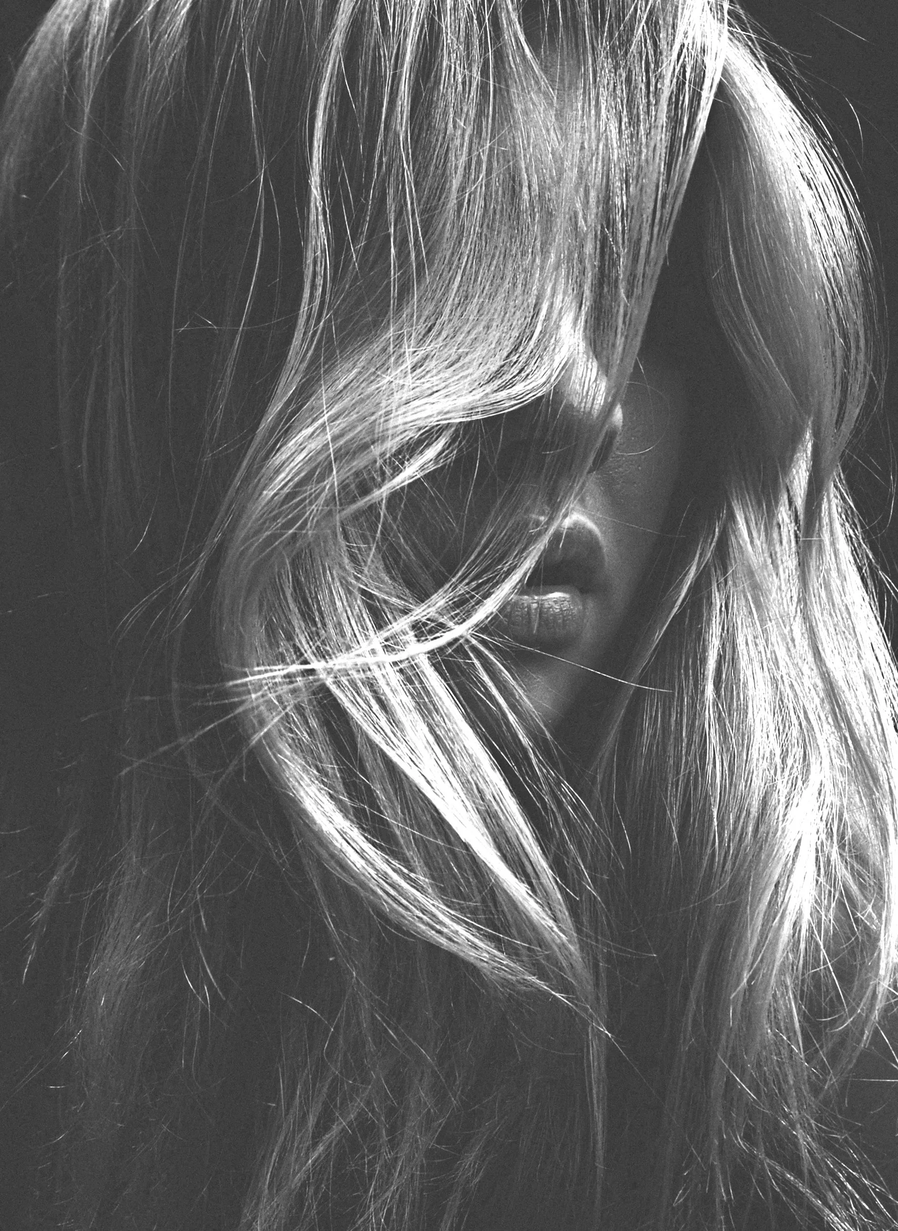 A black and white close-up photograph of a person's face partially obscured by windblown long, wavy hair.