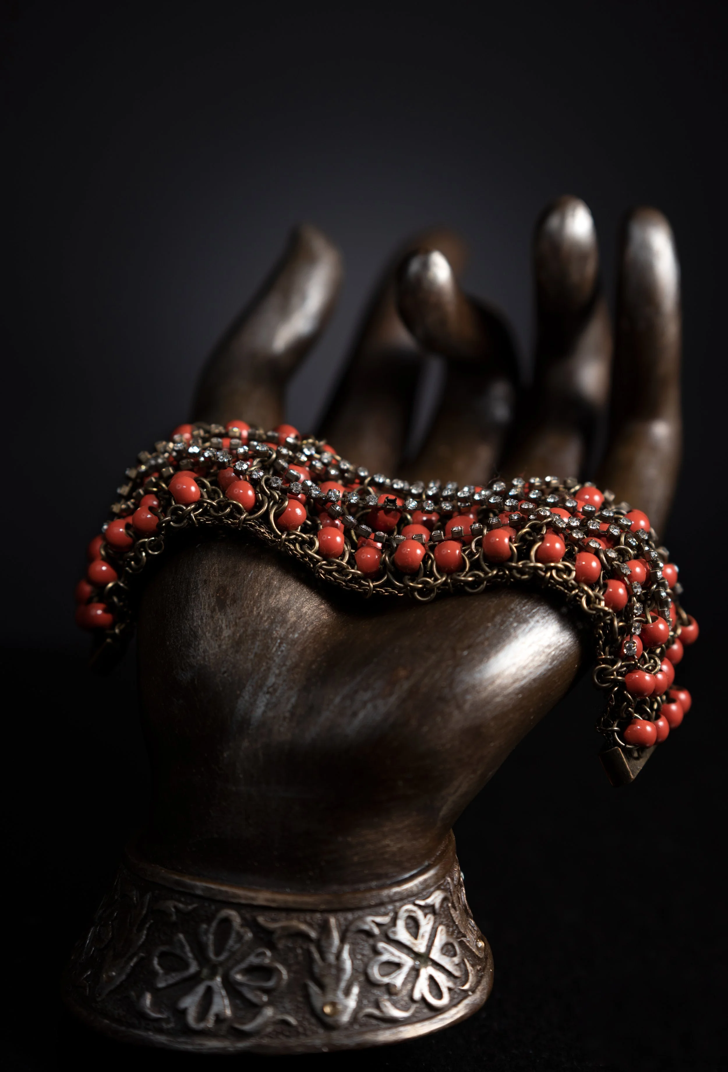 A dark bronze color hand-shaped jewelry display with a necklace draped over it, featuring coral beads and small clear crystals.
