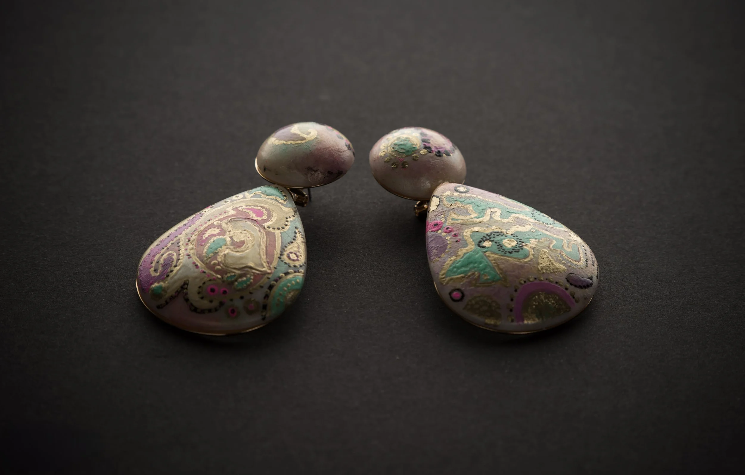 Decorative earrings with pastel-colored swirling patterns against a dark background.