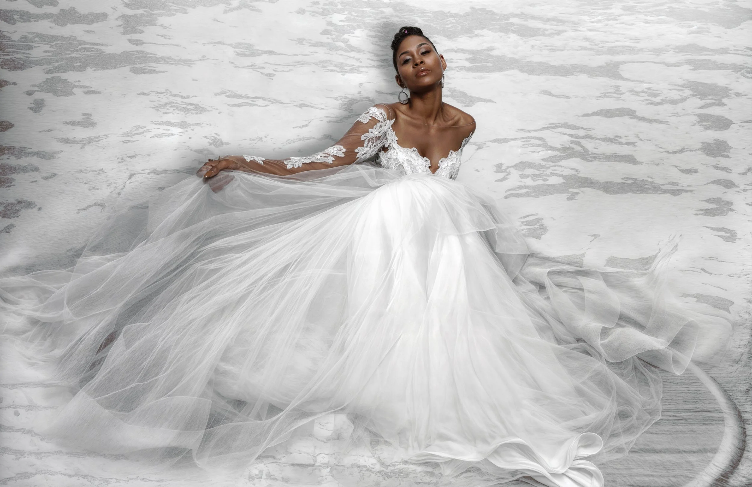 A woman in a white wedding gown with lace and sheer long sleeves, sitting on the floor with a snowy or icy background.