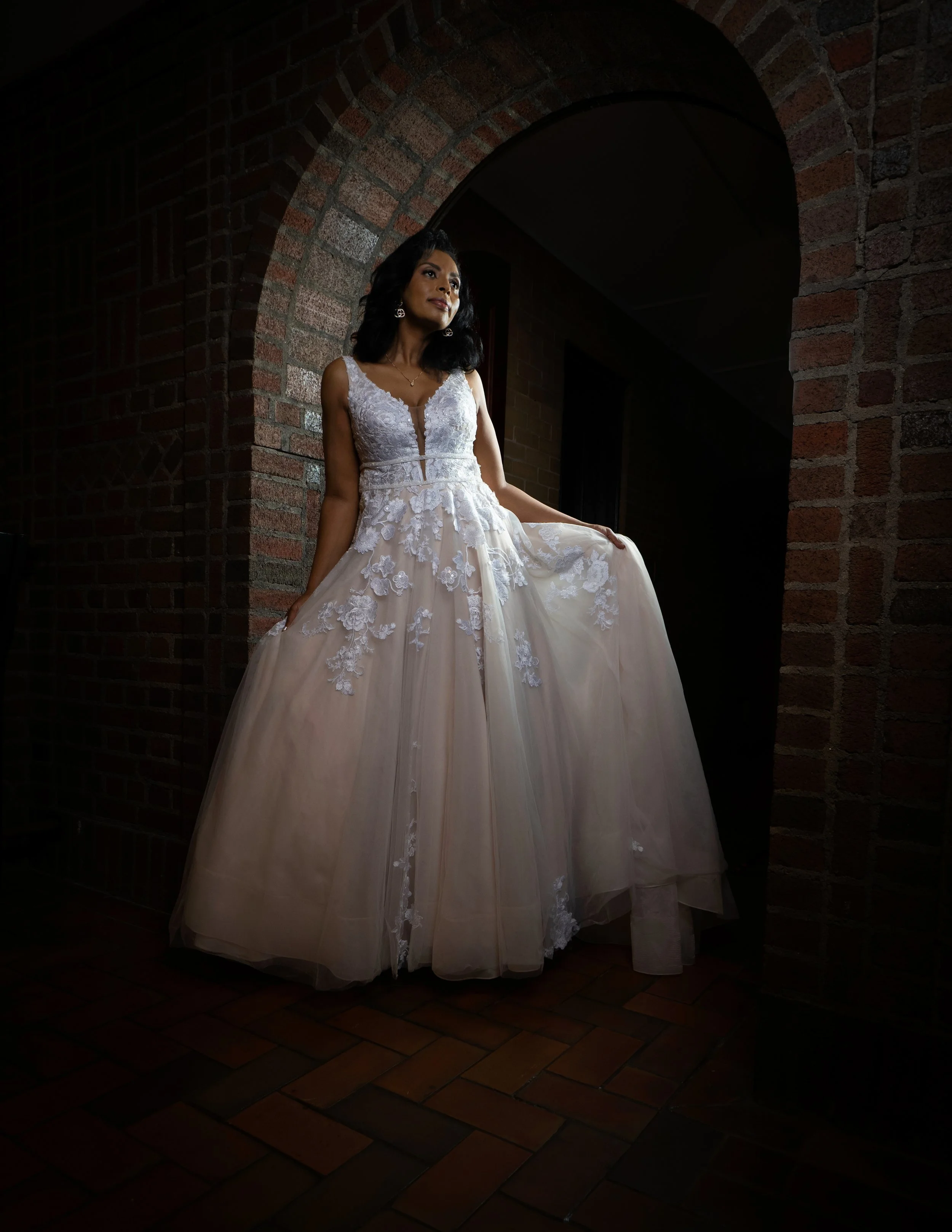 Women in a wedding dress standing under an archway with brick walls visible.