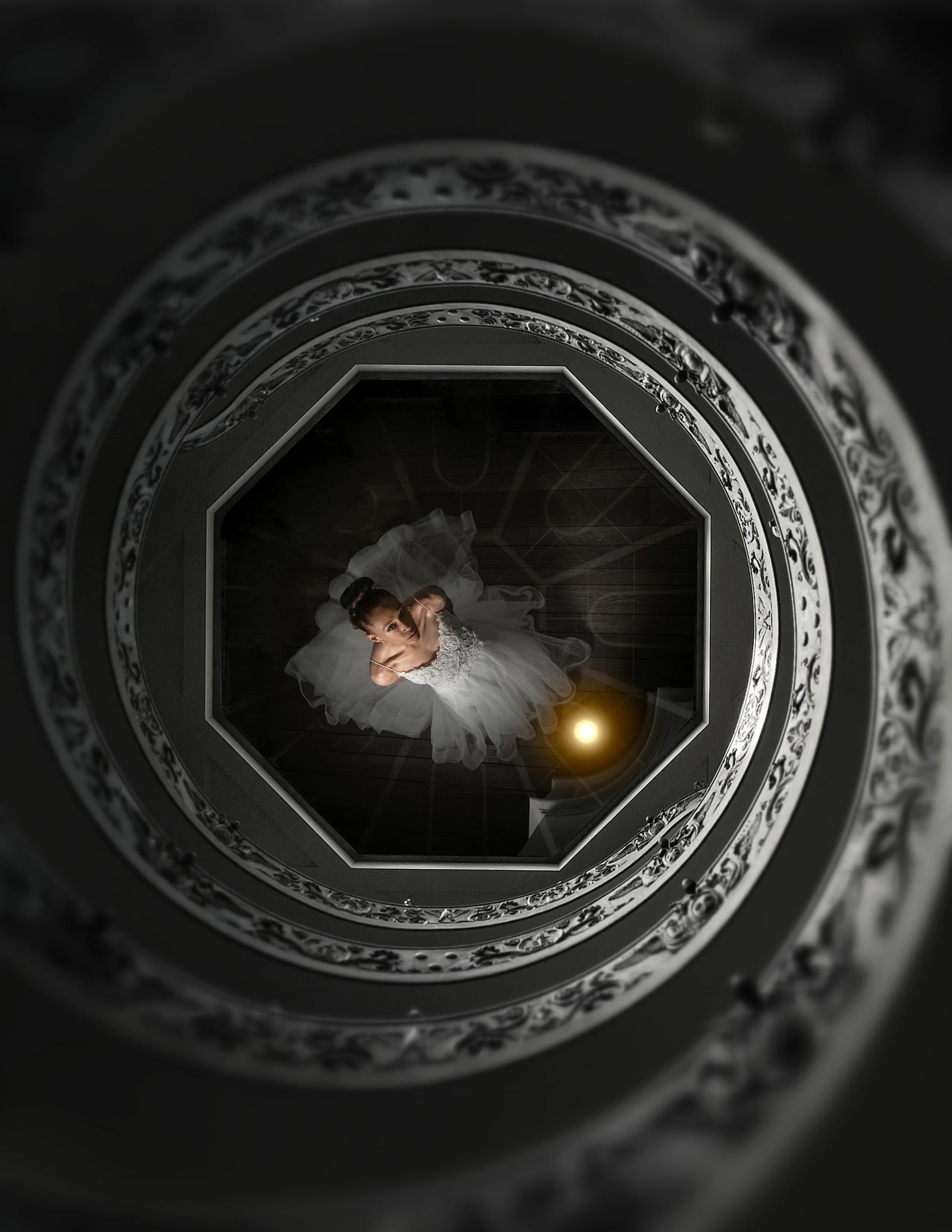 A woman in a white wedding dress looking up at the camera from the bottom of a spiral staircase with ornate railings.