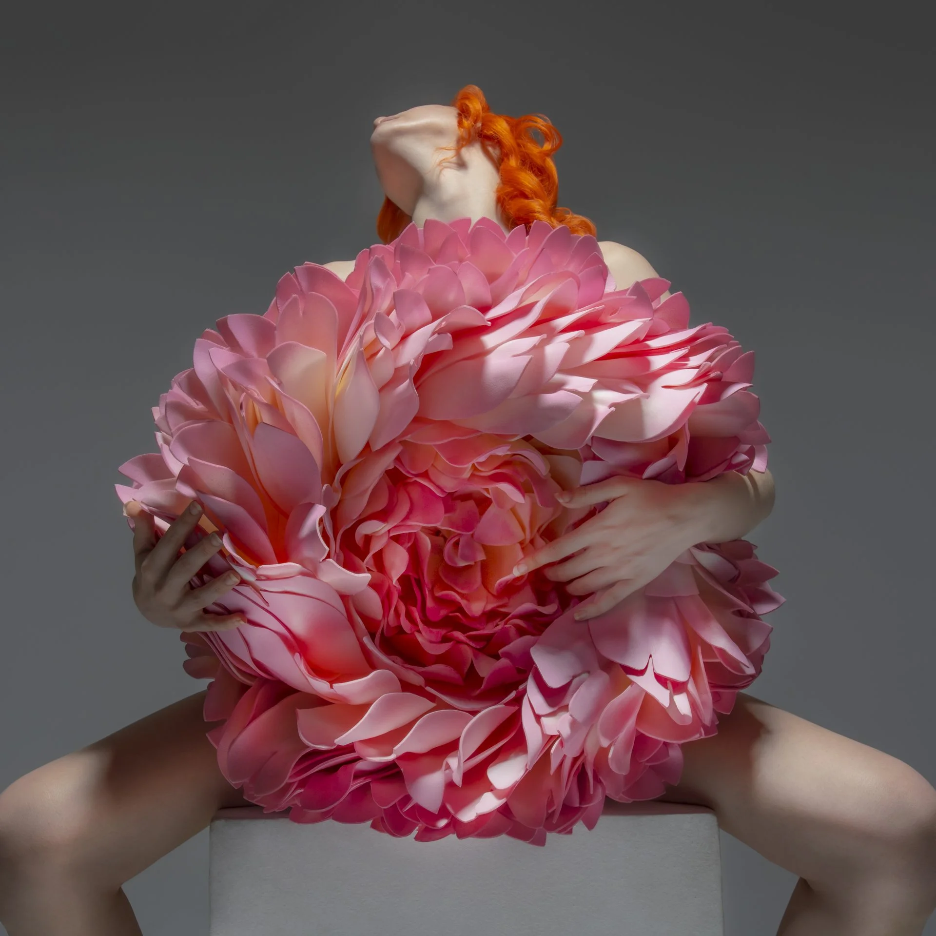 Person with orange hair holding a large pink flower resembling a peony.