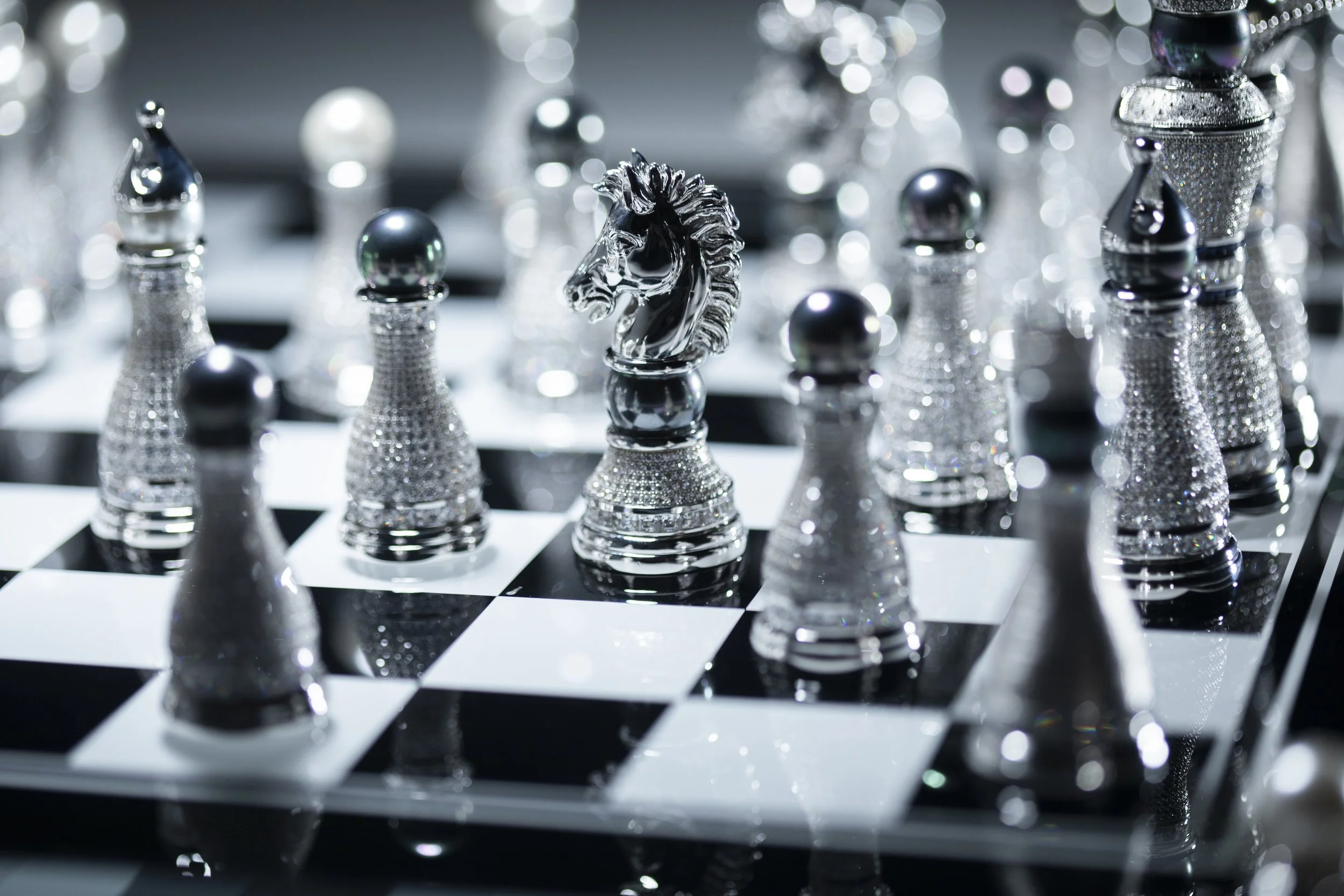 A shiny chess set with silver chess pieces on a black and white checkered board, featuring a detailed horse head piece in the center.