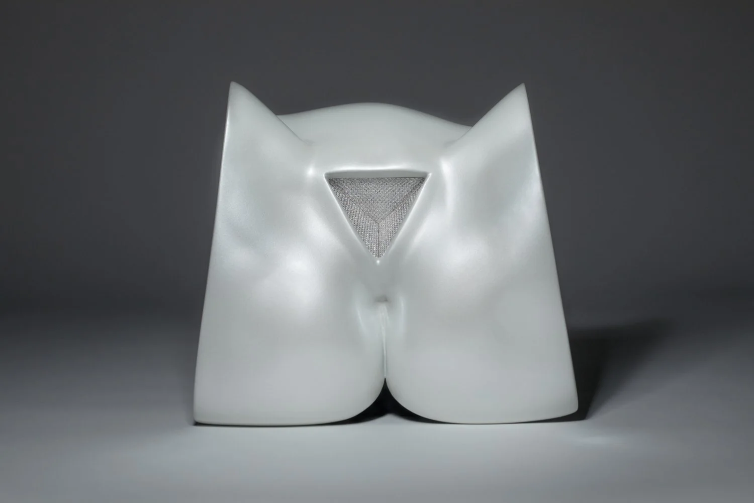 A white object with a triangular opening in the center, shaped like an abstract sculpture or modern art piece, set against a dark and light gradient background.