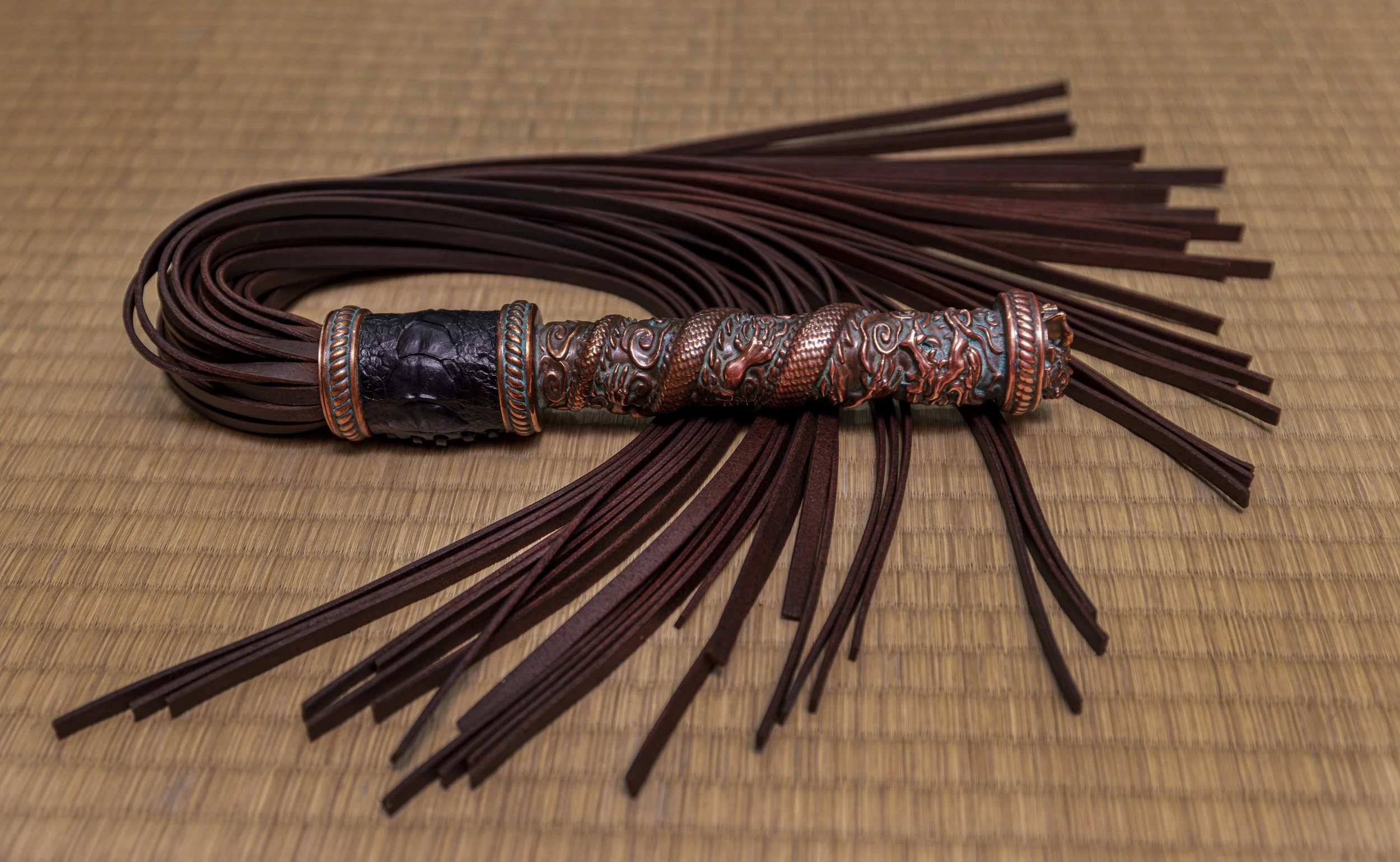 A leather whip with a decorated handle, laying on a woven mat.