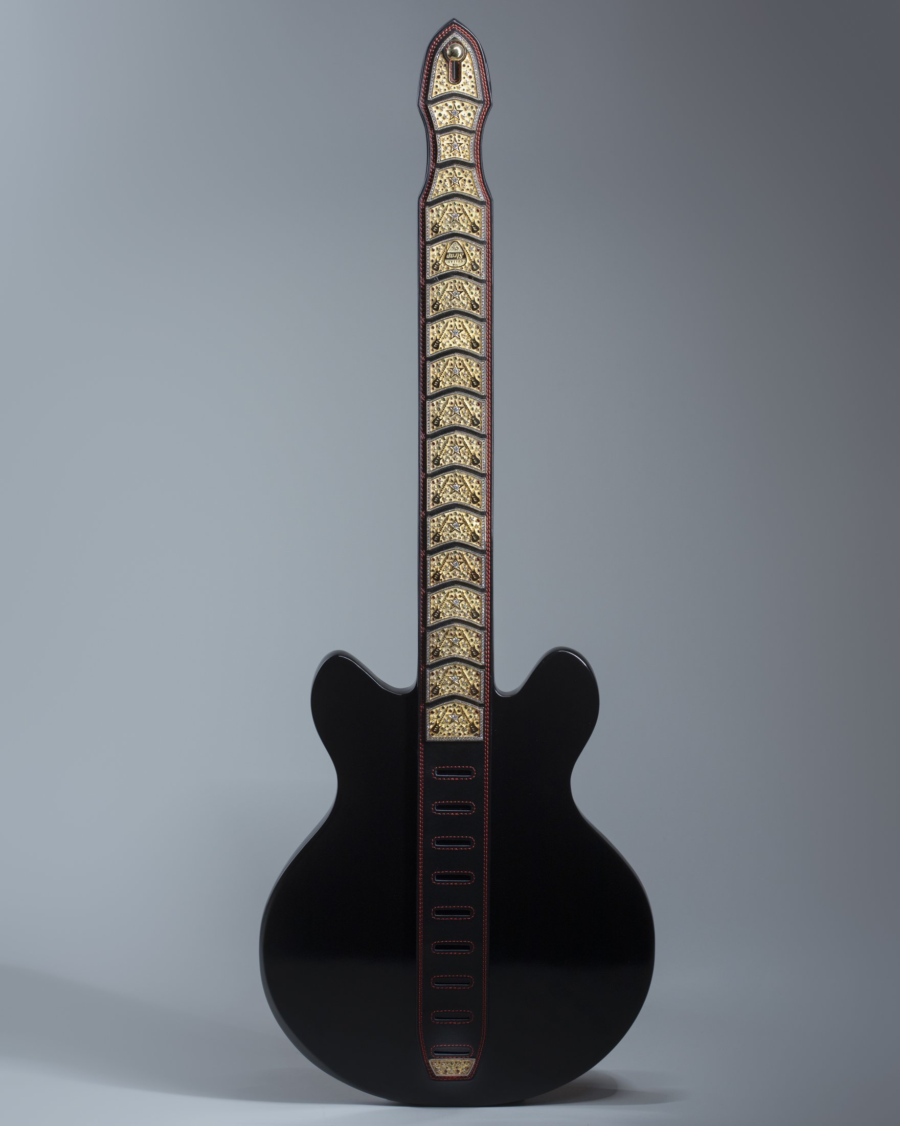 Black electric guitar with gold decorative fretboard, photographed against a plain gray background.