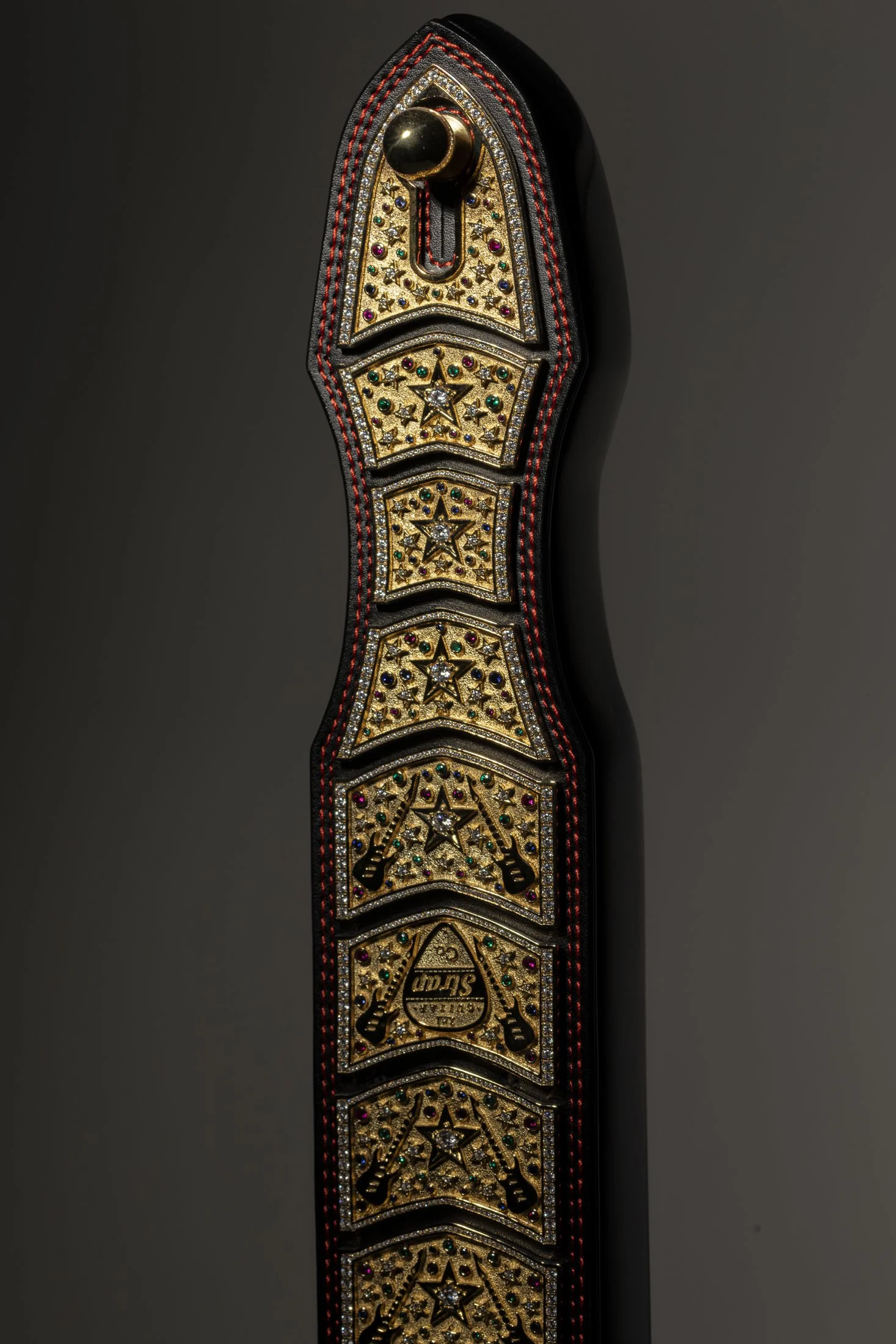 Close-up of a decorated guitar strap with gold, star, and gemstone embellishments.