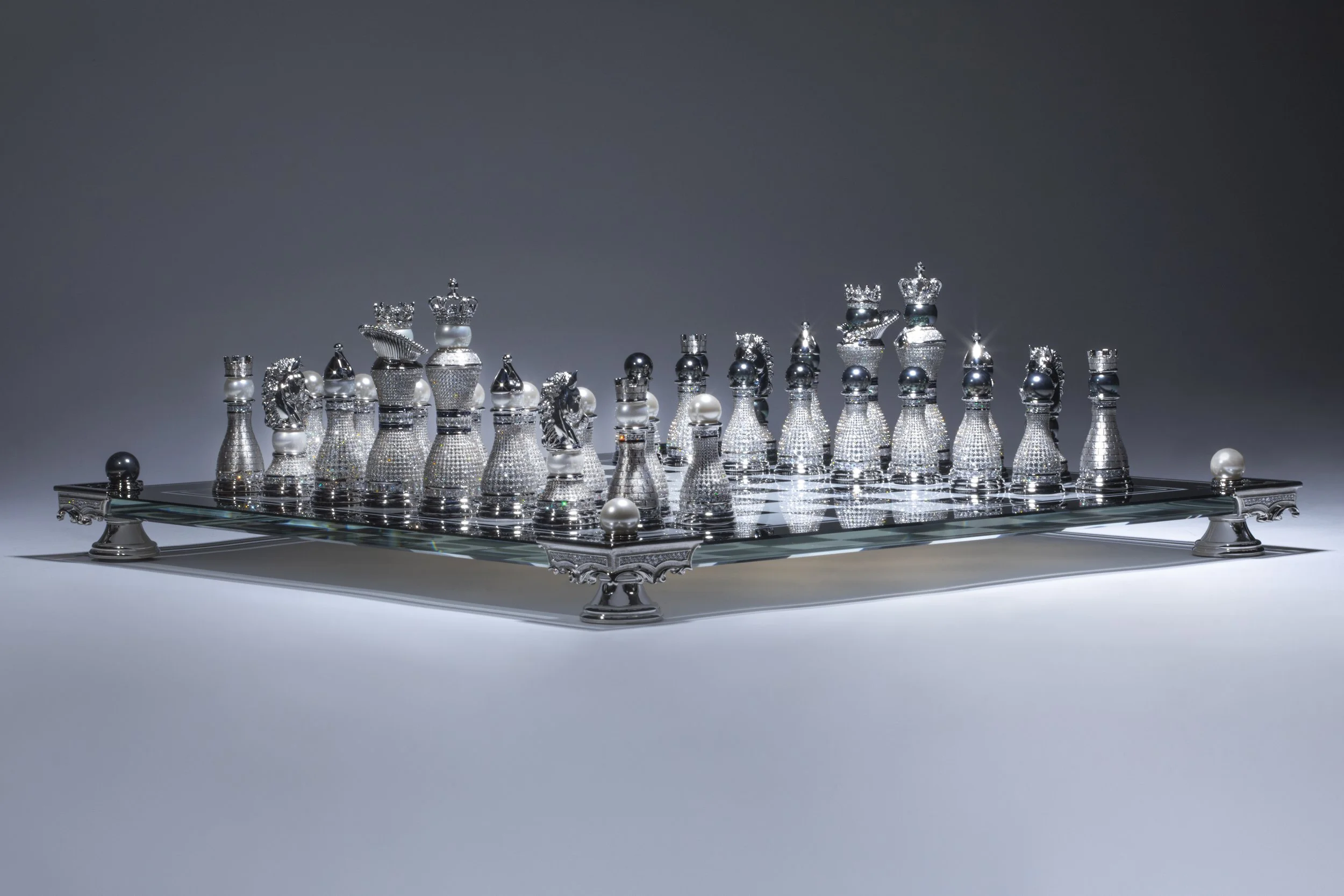 Luxury chess set with metallic and pearl pieces on a glass board with ornate metallic legs