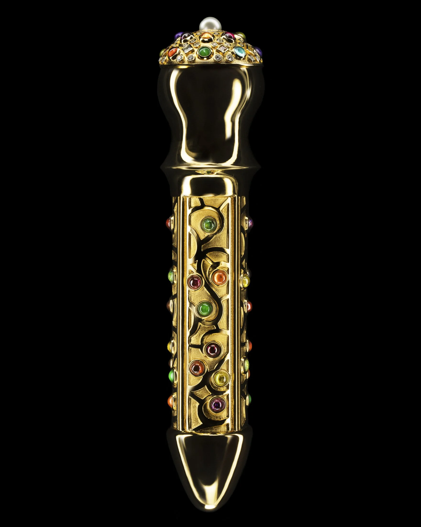 A decorative gold object with colorful gemstones, resembling an ornate pen or ceremonial piece, set against a black background.