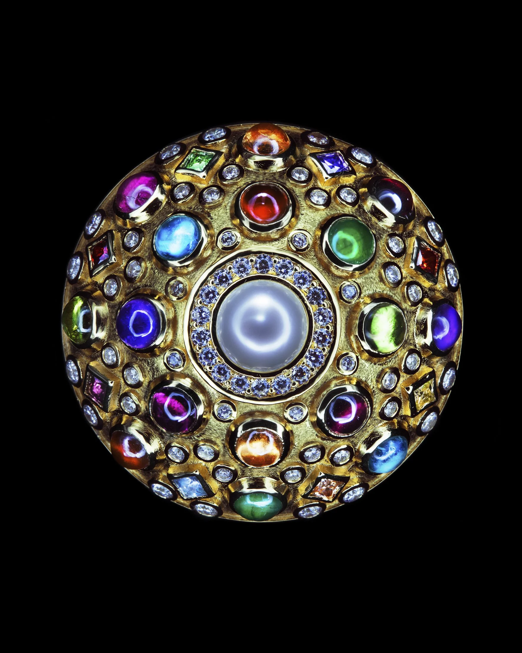 A circular jewelry piece with multicolored gemstones set in gold, centered by a large white pearl surrounded by small diamonds, all against a black background.