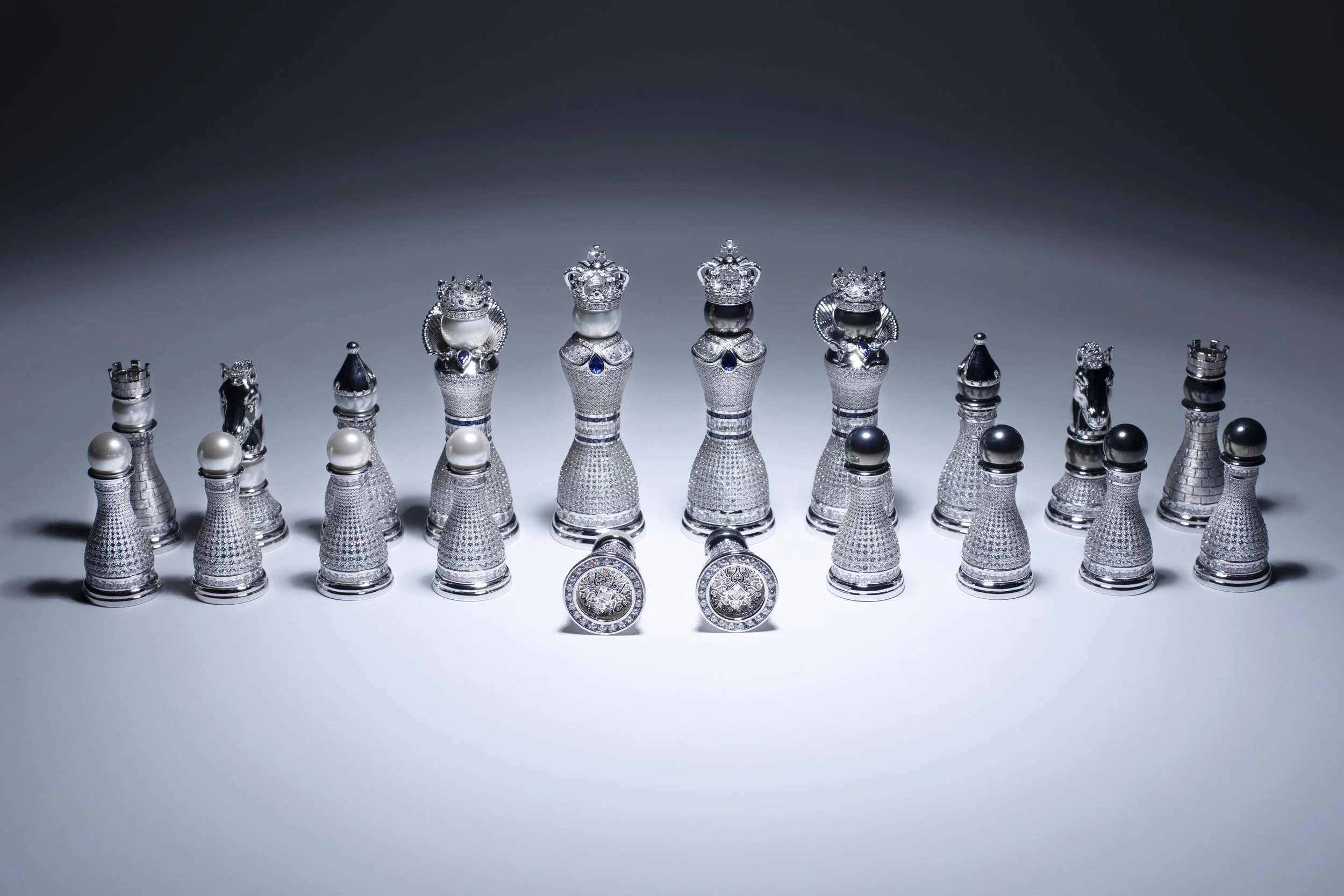 Luxury chess set with silver, jeweled pieces, arranged on a light surface against a dark background.