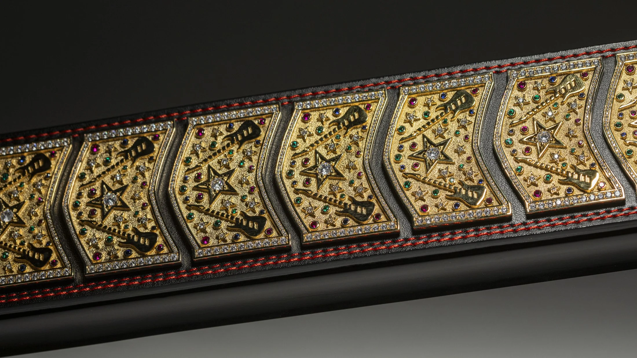 Close-up of a black belt with gold, diamond, and colorful gemstone embellishments, featuring various star shapes and intricate designs.