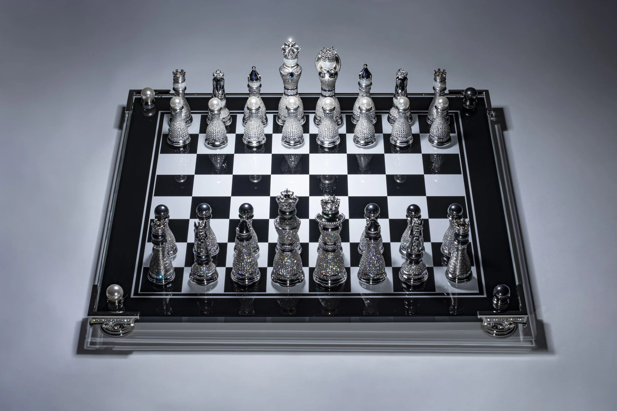 A luxury chess set with metallic and jewel-encrusted pieces on a black and white chessboard.