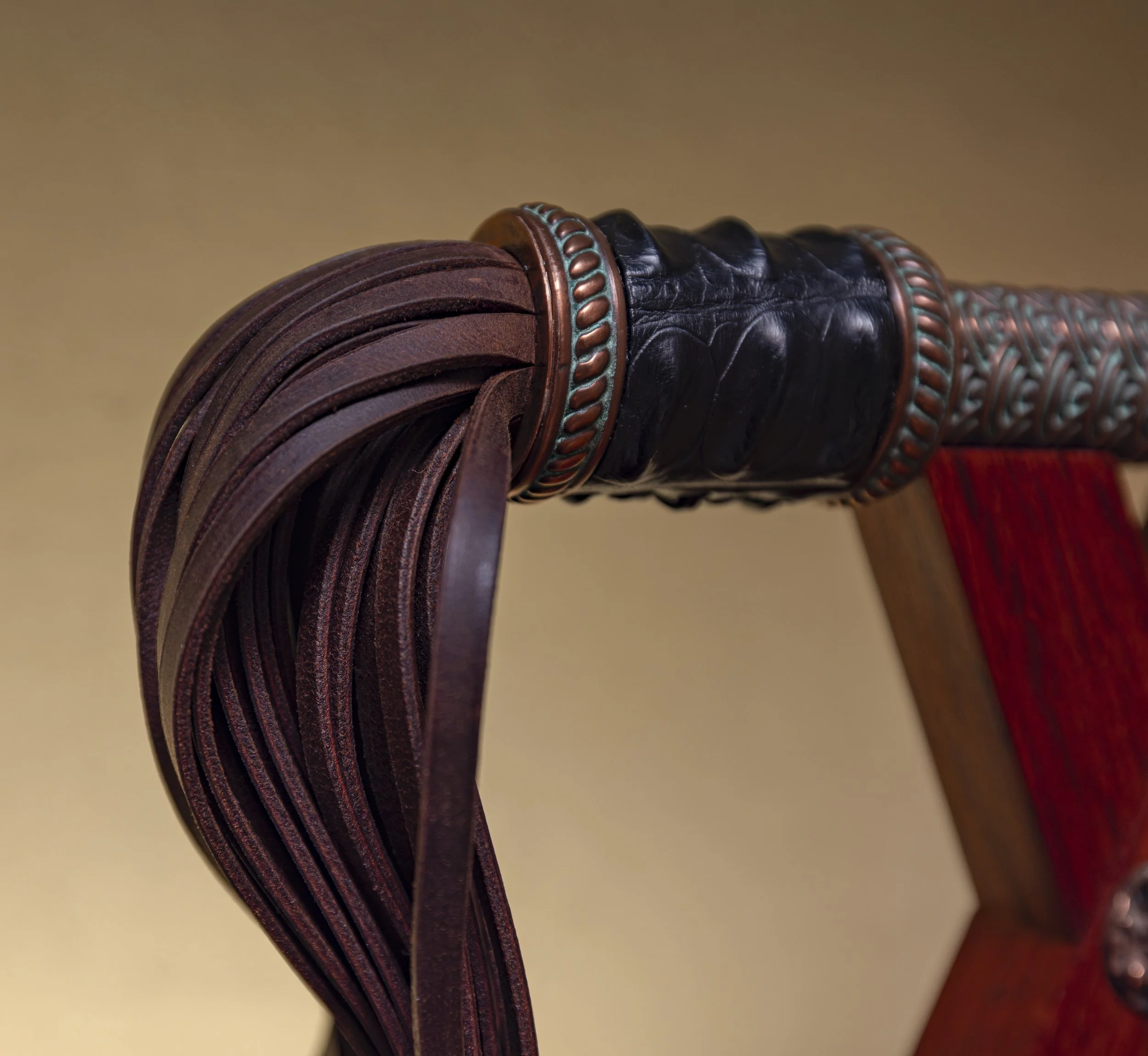 Close-up of a chair's wooden frame with detailed leather and metal accents, and leather straps hanging from the top.