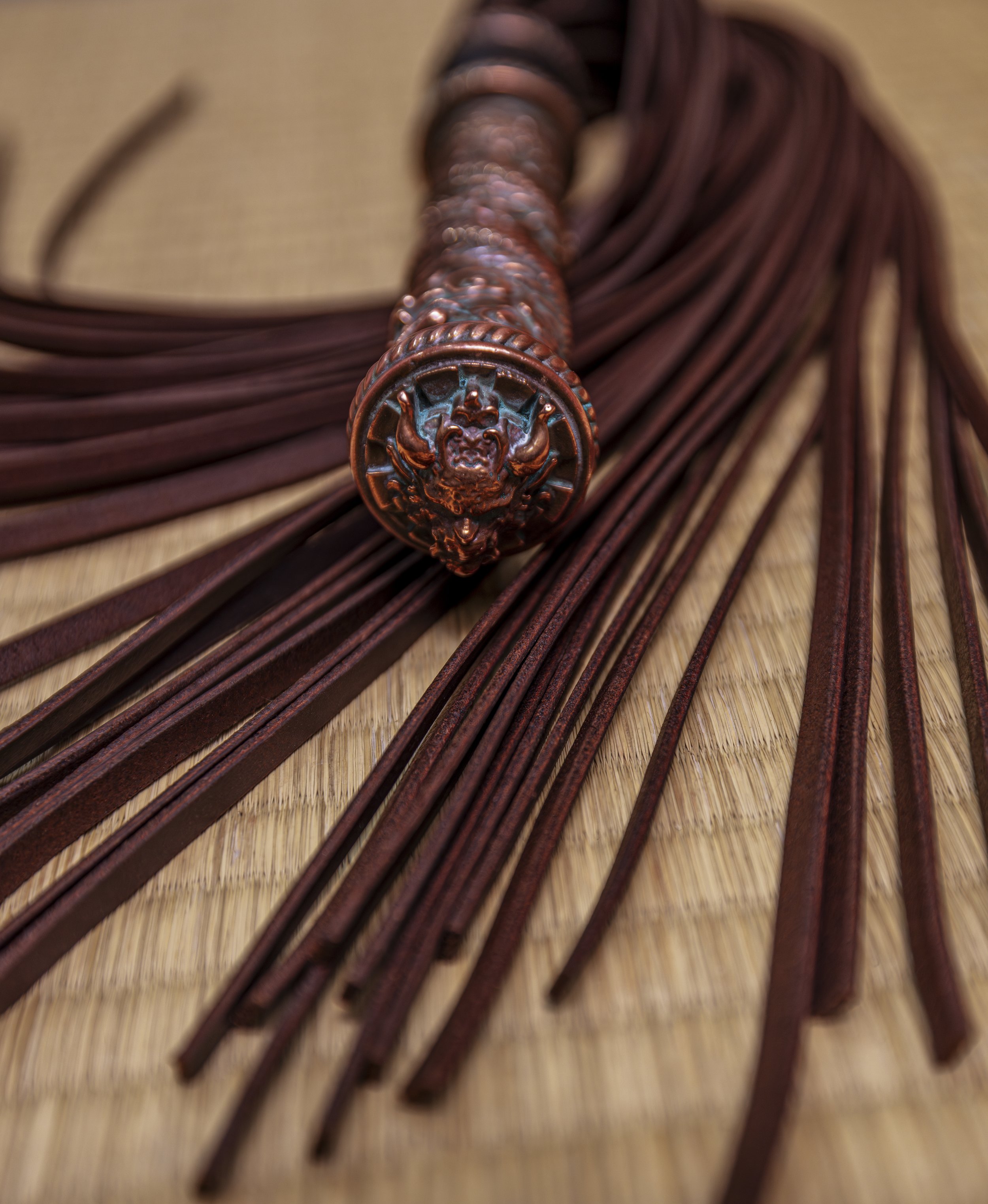 Close-up of a copper ceremonial dagger with a decorative handle and multiple leather strips attached, resting on a woven mat.