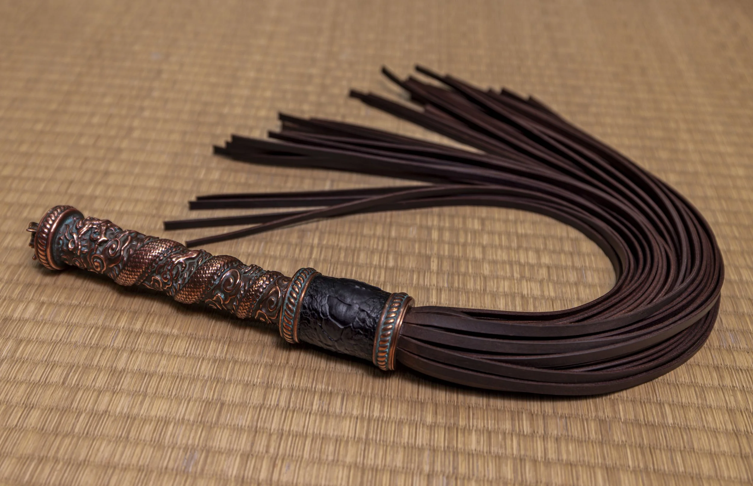 Whip with a decorative handle and leather lash on a wooden surface.