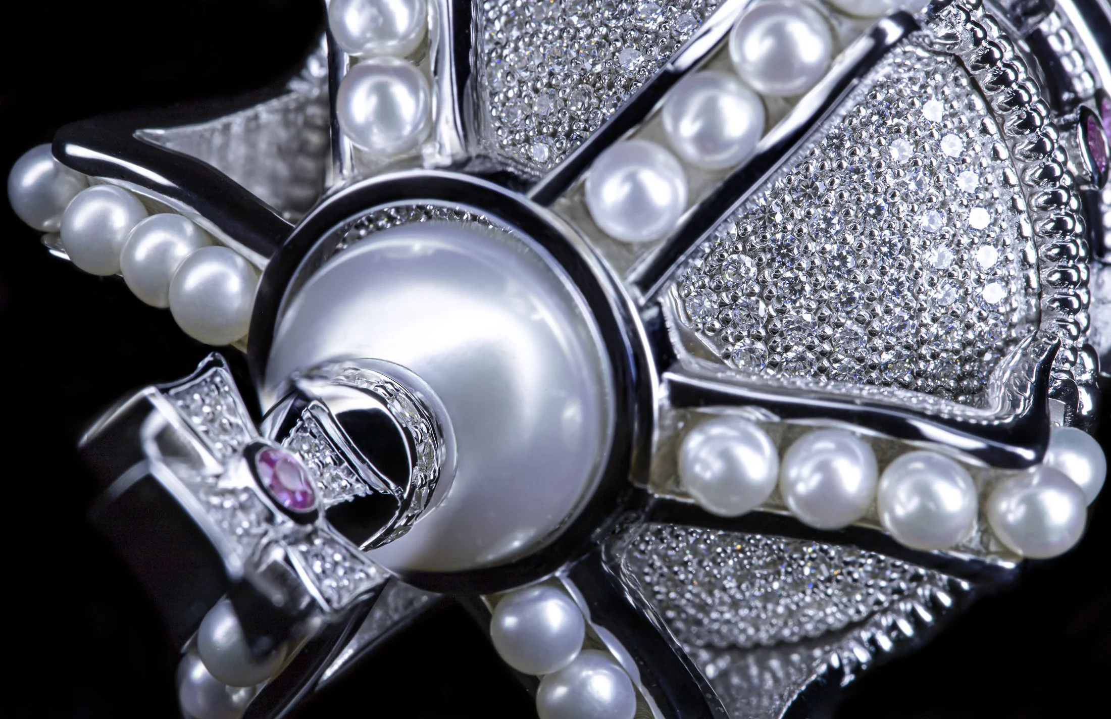 Close-up of a jewelry piece with pearls, rhinestones, and a large pearl centerpiece, set in metallic elements with a pink gemstone accents.