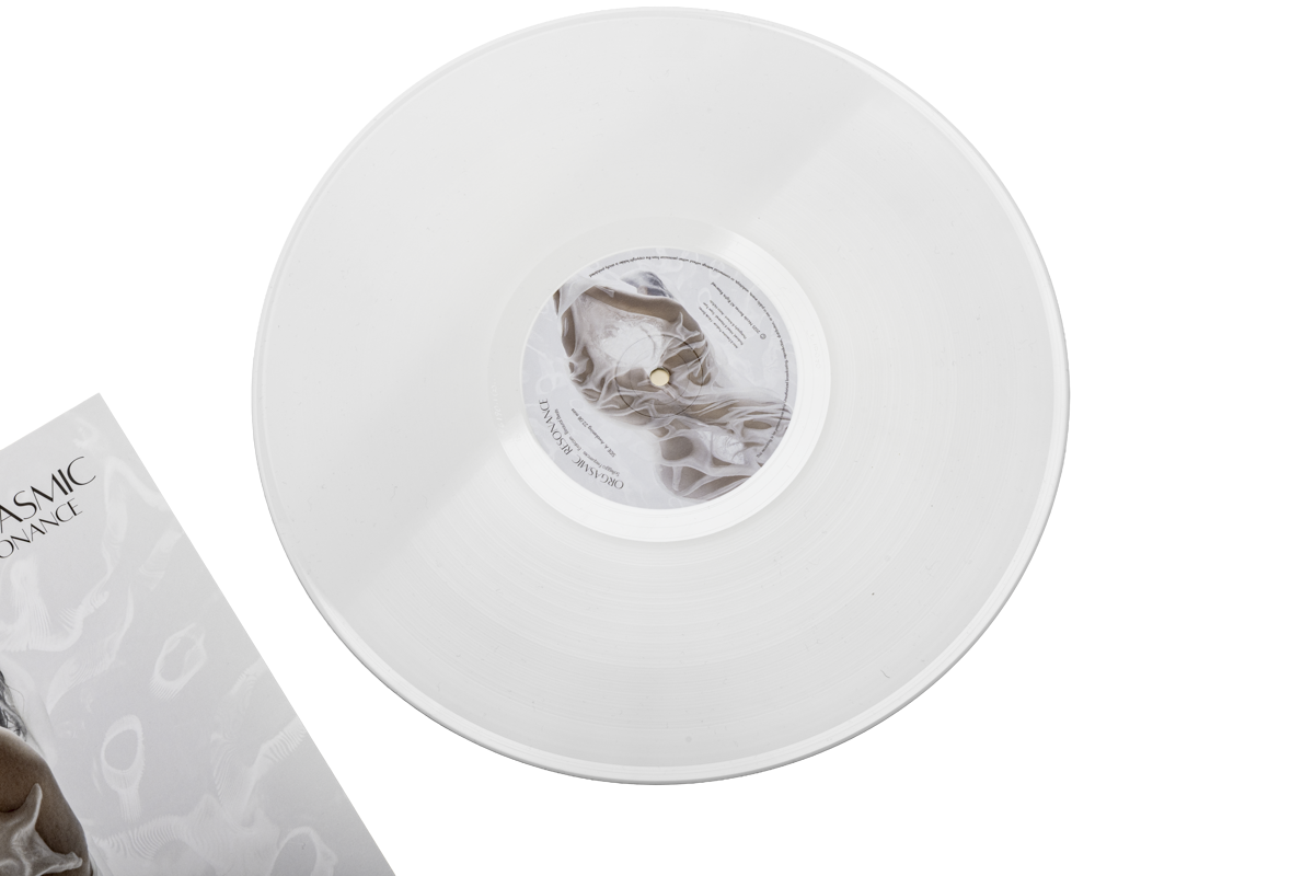 A white vinyl record on a gray surface, partially inside a white box with yellow accents, with a label featuring abstract gray and white designs.