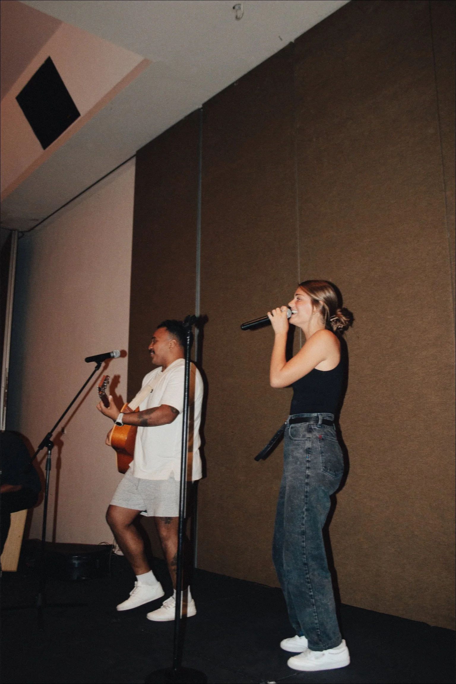 A woman singing into a microphone and a man playing a guitar on stage during a live performance.