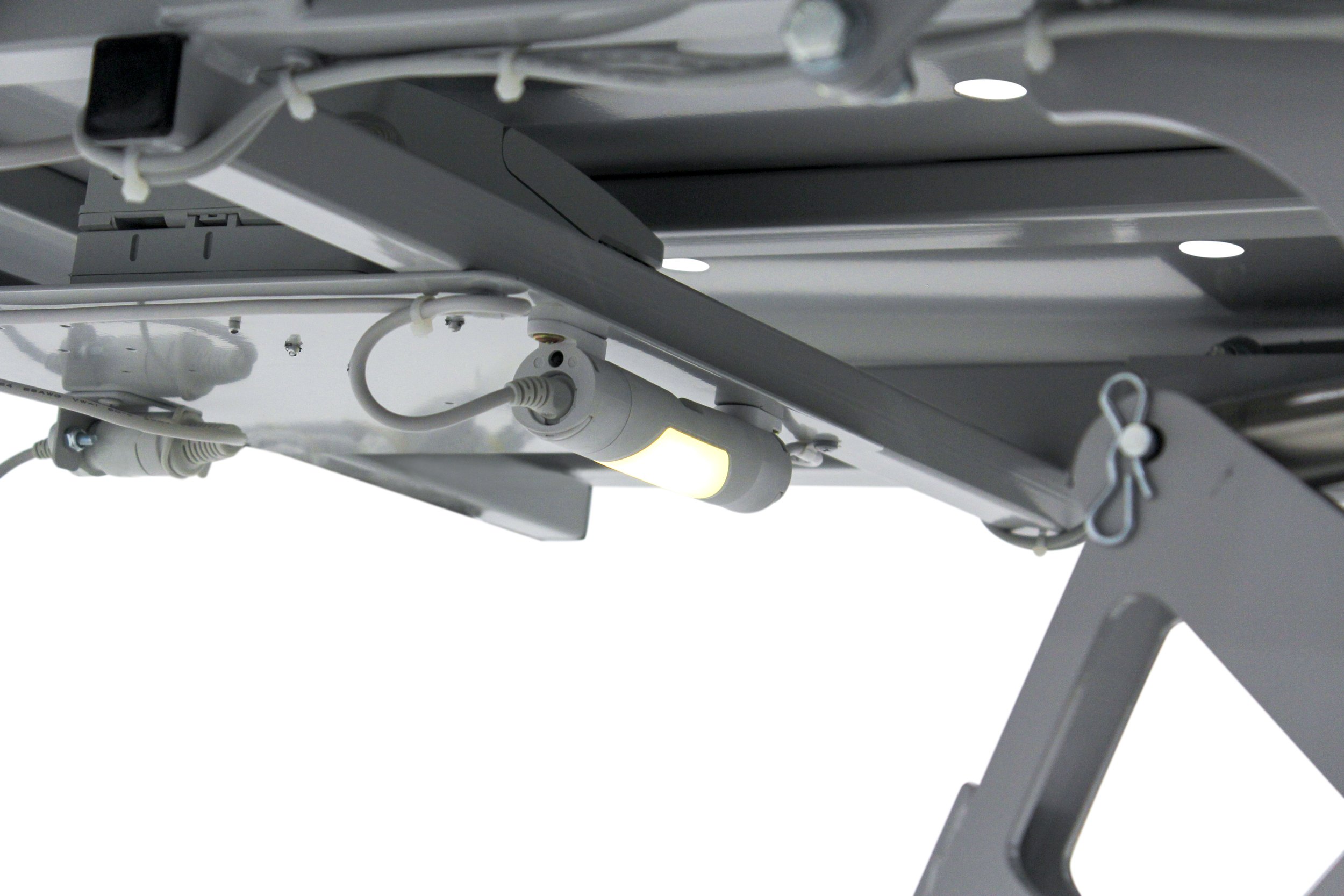 Close-up of the underside of a metallic medical or dental examination table, showing cables, screws, and a light or electrical component attached beneath the table surface.