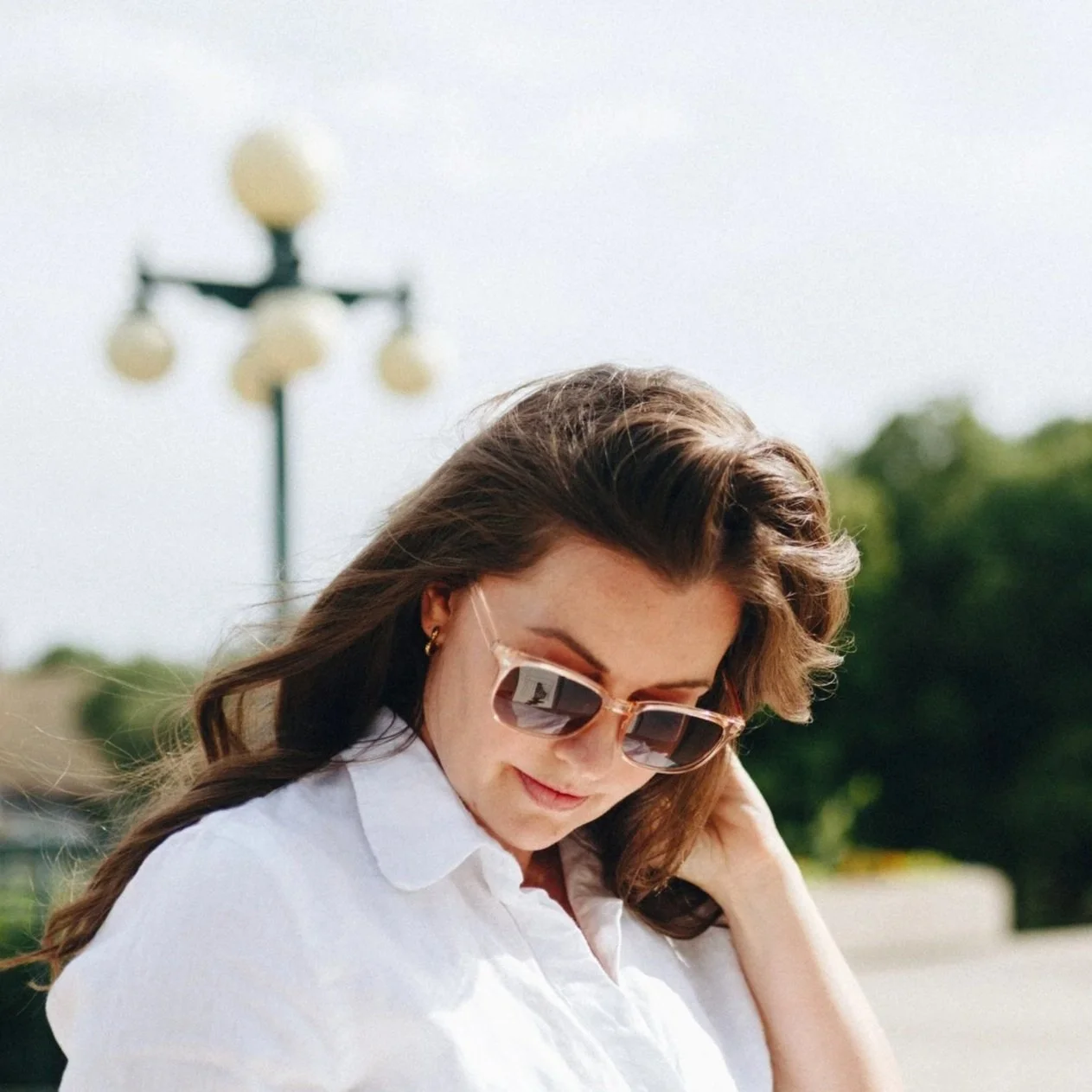 A woman wearing sunglasses and a white shirt outdoors on a sunny day.