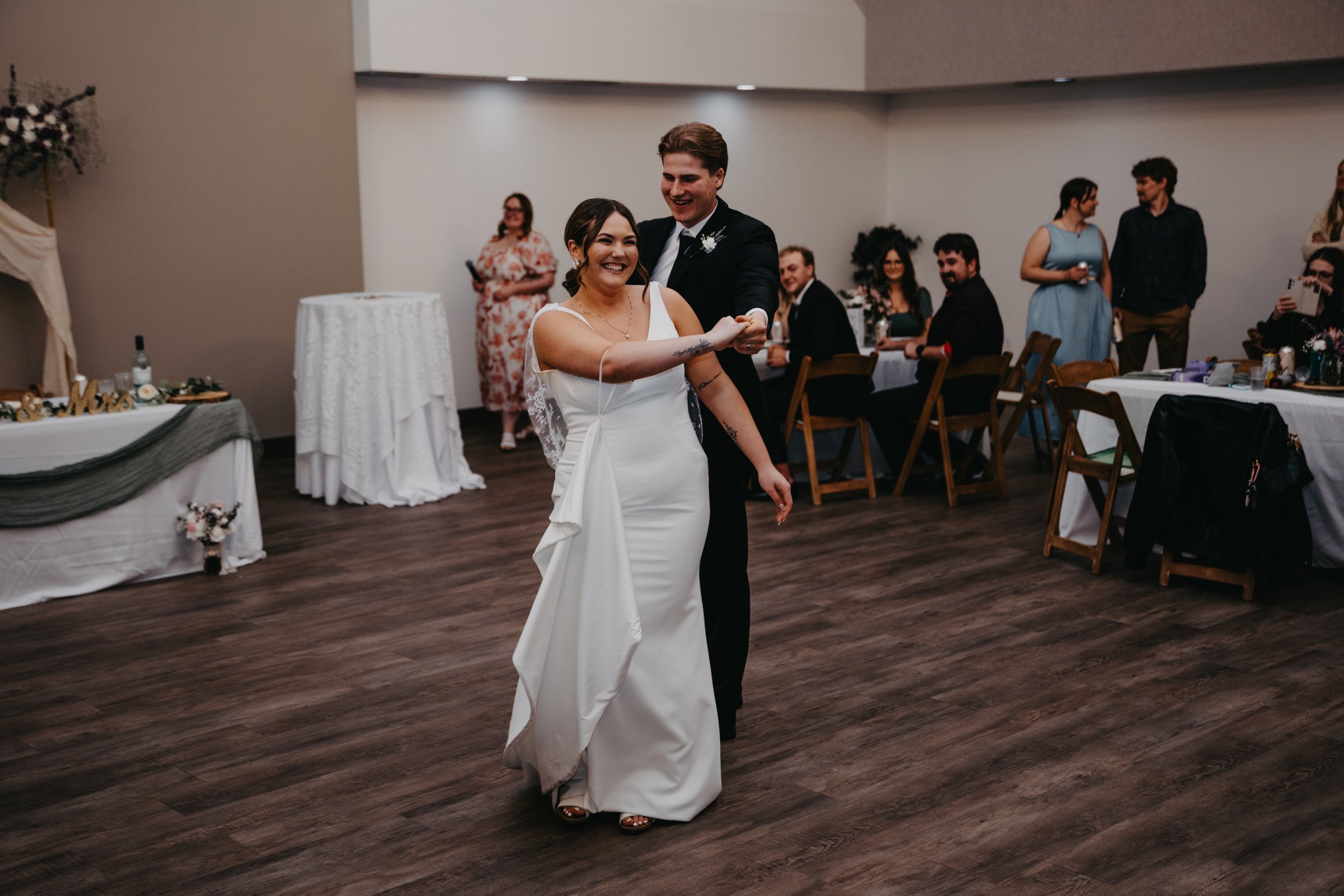 A couple dancing at a wedding reception, with guests watching and smiling in the background.