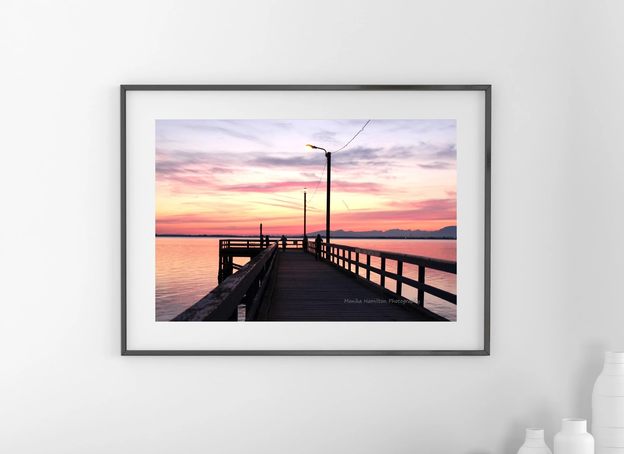 Sunset at Crescent Beach Pier in South Surrey, British Columbia - the pastel sky reflects on the calm water. There are silhouettes of the pier, lights, and people. Monika Hamilton Photography