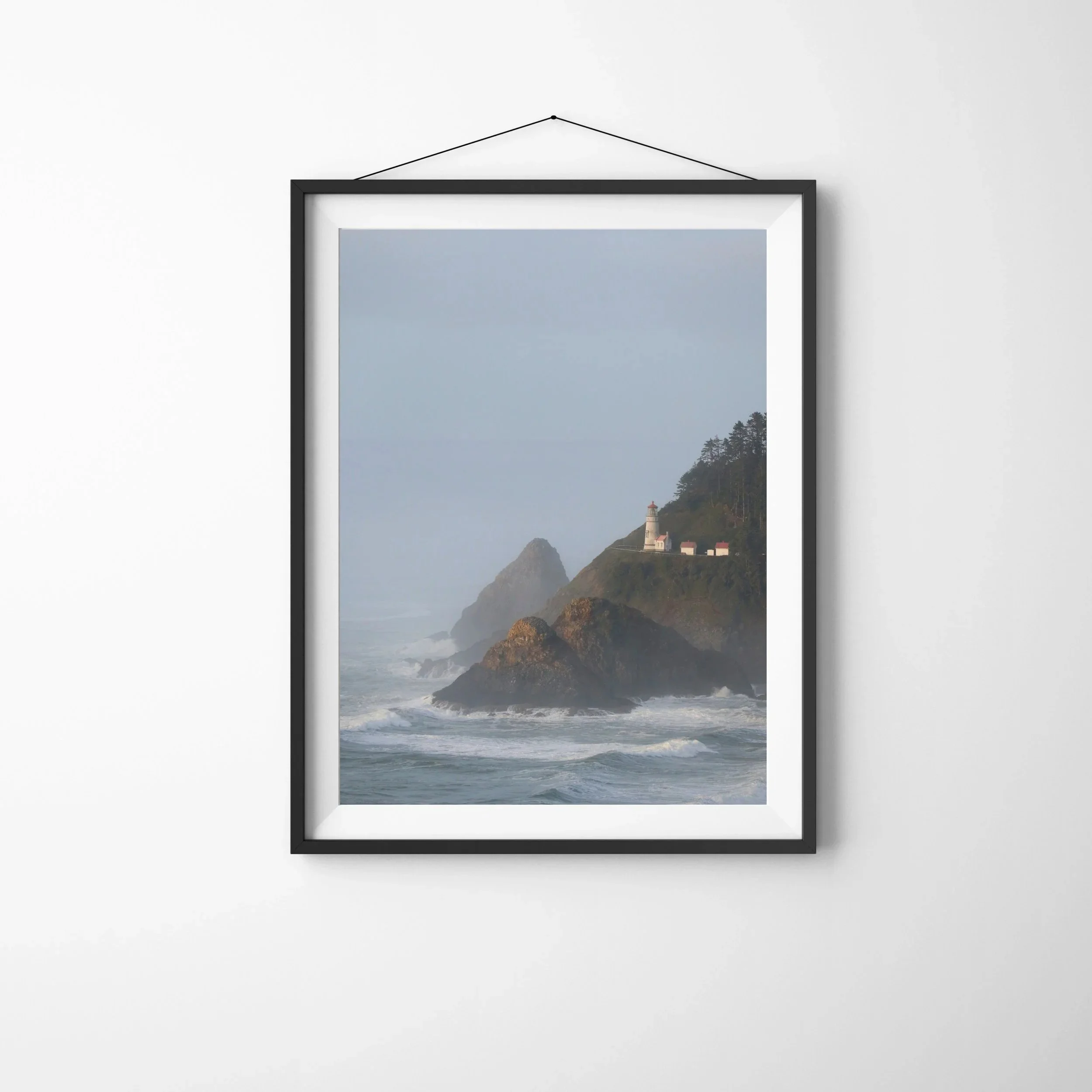 The Hecata Head Lighthouse on the Oregon Coast on a Misty Afternoon. The red and white lighthouse is perched on a rocky hillside overlooking the ocean. Monika Hamilton Photography