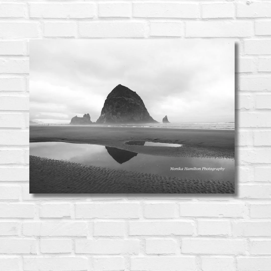 Cannon Beach's Haystack Rock reflects in the water of a tide pool on the Oregon Coast in this black and white photograph.