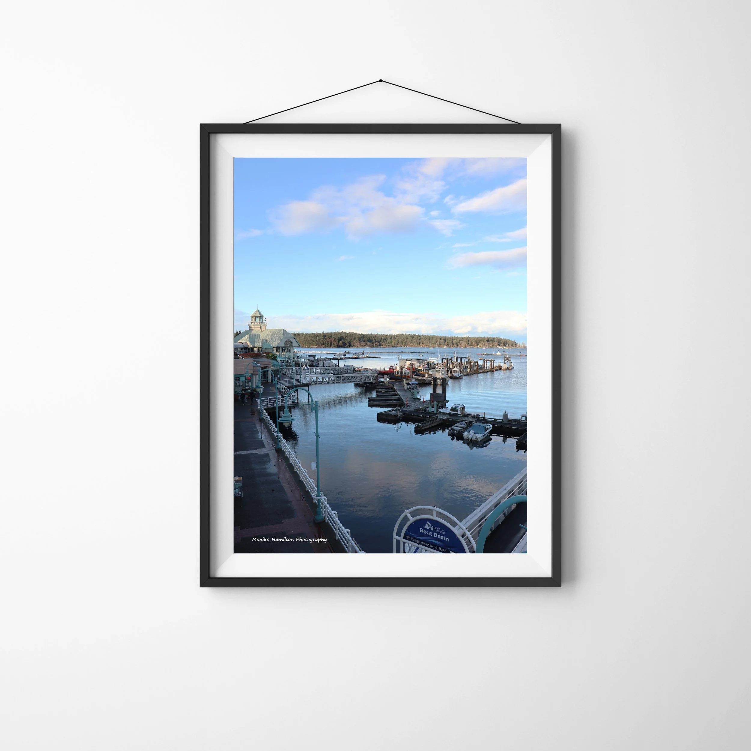 Sunset at Nanaimo's Waterfront Marina with boats docked, the walkway with shops and restaurants, and clouds reflecting in the calm blue water. Monika Hamilton Photography