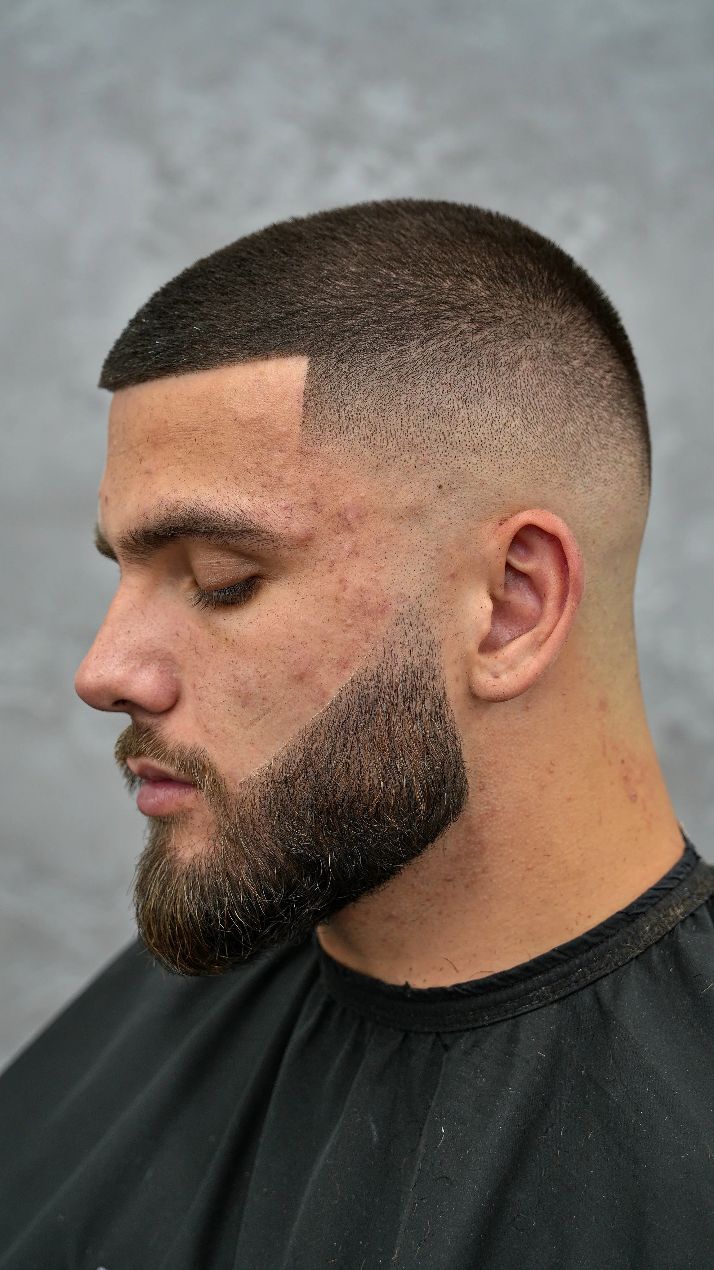 Close-up of a man with a fresh skin fade haircut and a full beard, sitting in a barbershop.