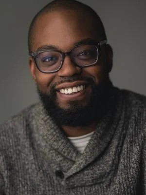 Smiling man with glasses and a beard wearing a gray sweater.