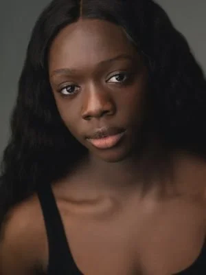 Portrait of a young Black woman with long, wavy hair wearing a black top.