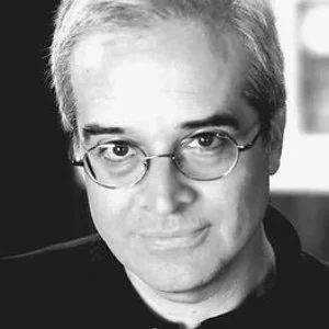 Black and white close-up photo of a man with glasses and gray hair, looking at the camera.