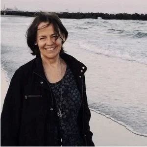 A woman smiling at the camera on a beach, with waves in the background.