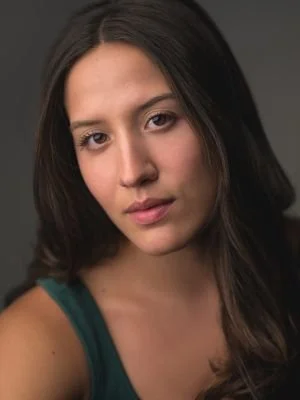 A portrait of a young woman with dark hair and a serious expression, wearing a dark green tank top, against a dark background.