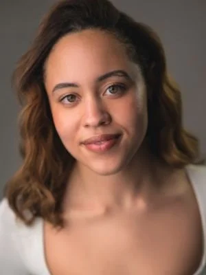 A young woman with wavy brown hair and light skin, smiling slightly, looking directly at the camera.